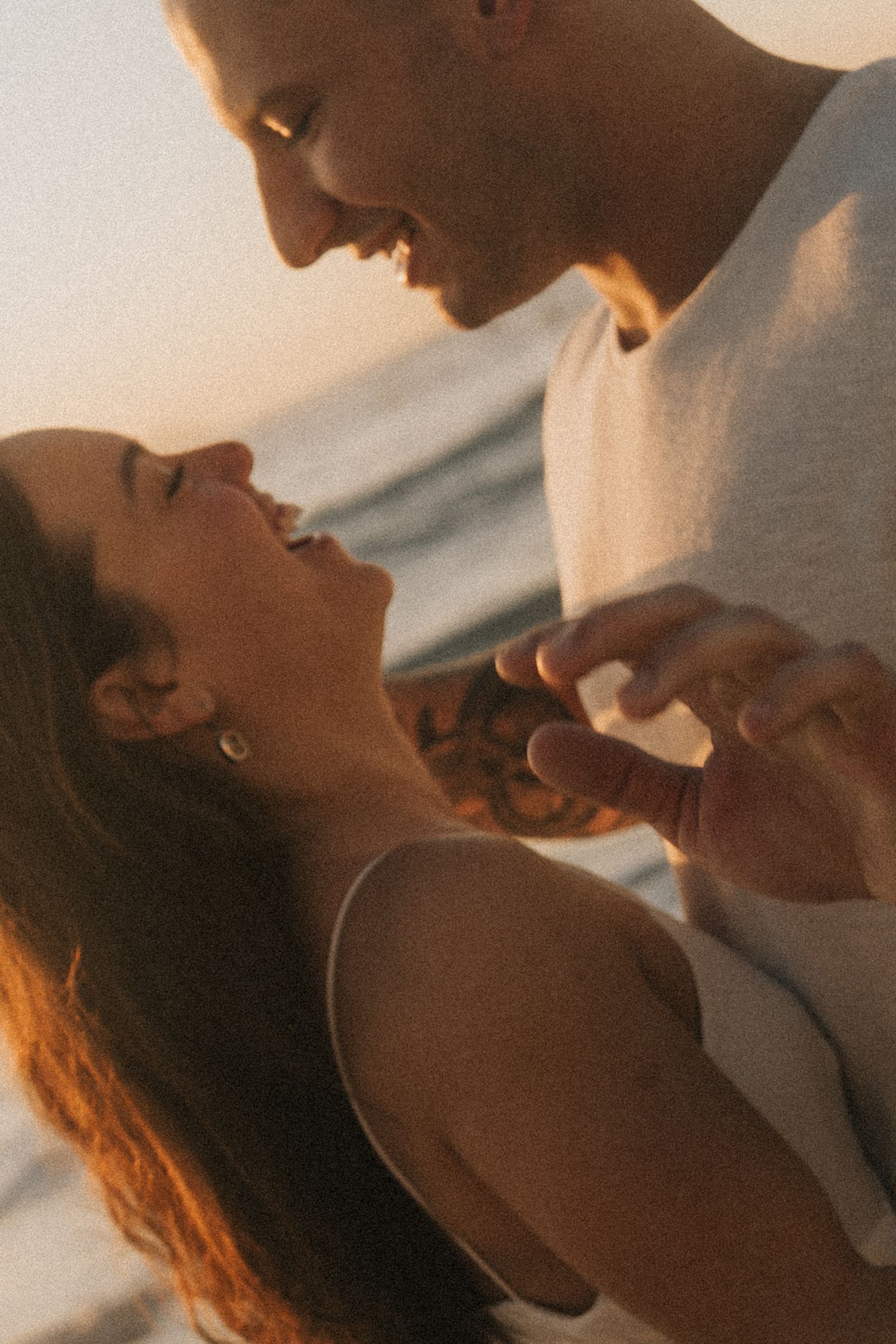 Intimate couple embraces in warm sunlight while holding hands and gazing at each other with affection.