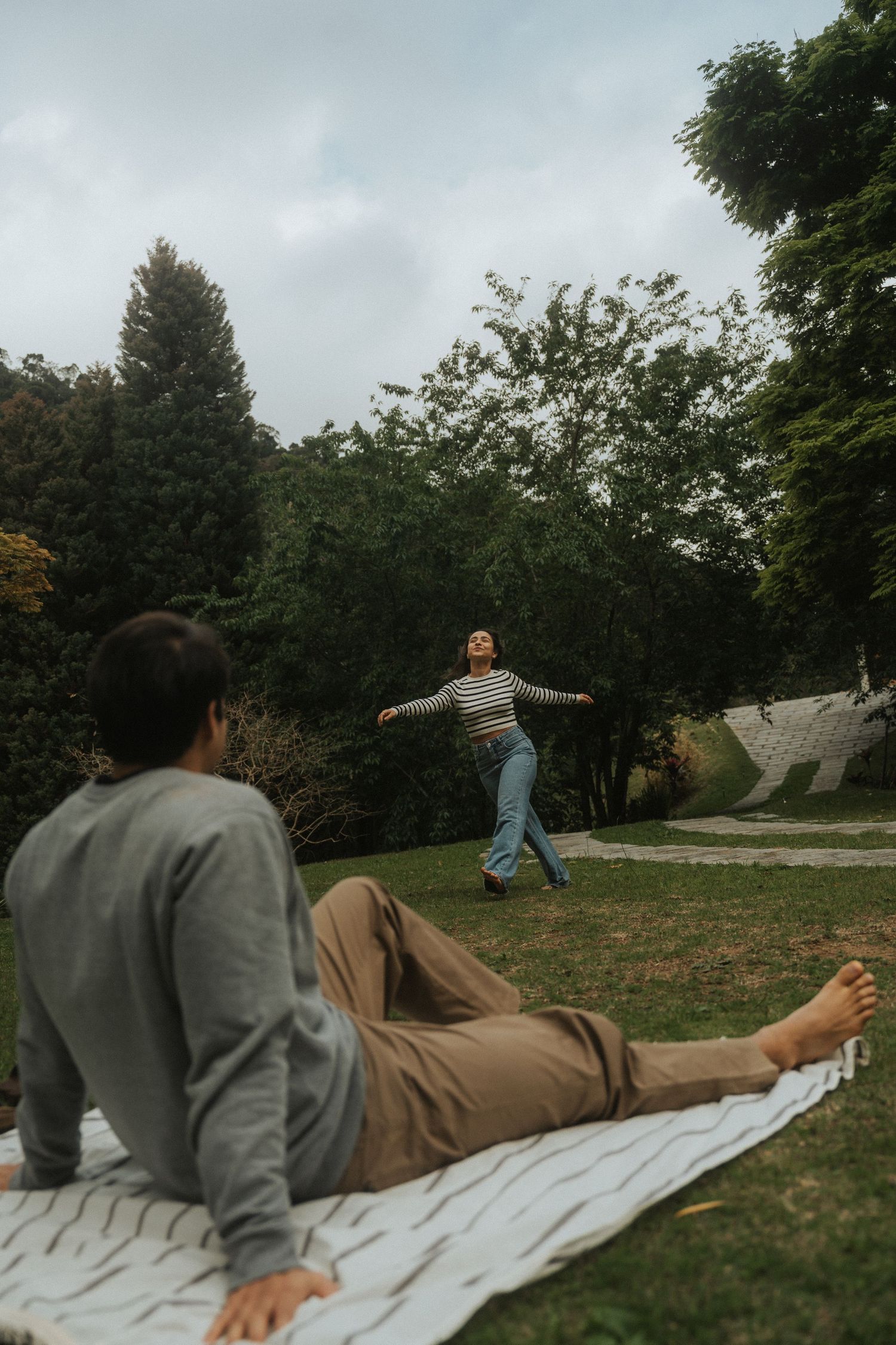 Two people enjoying a relaxing day outdoors on a blanket in a backyard garden setting on an overcast day.