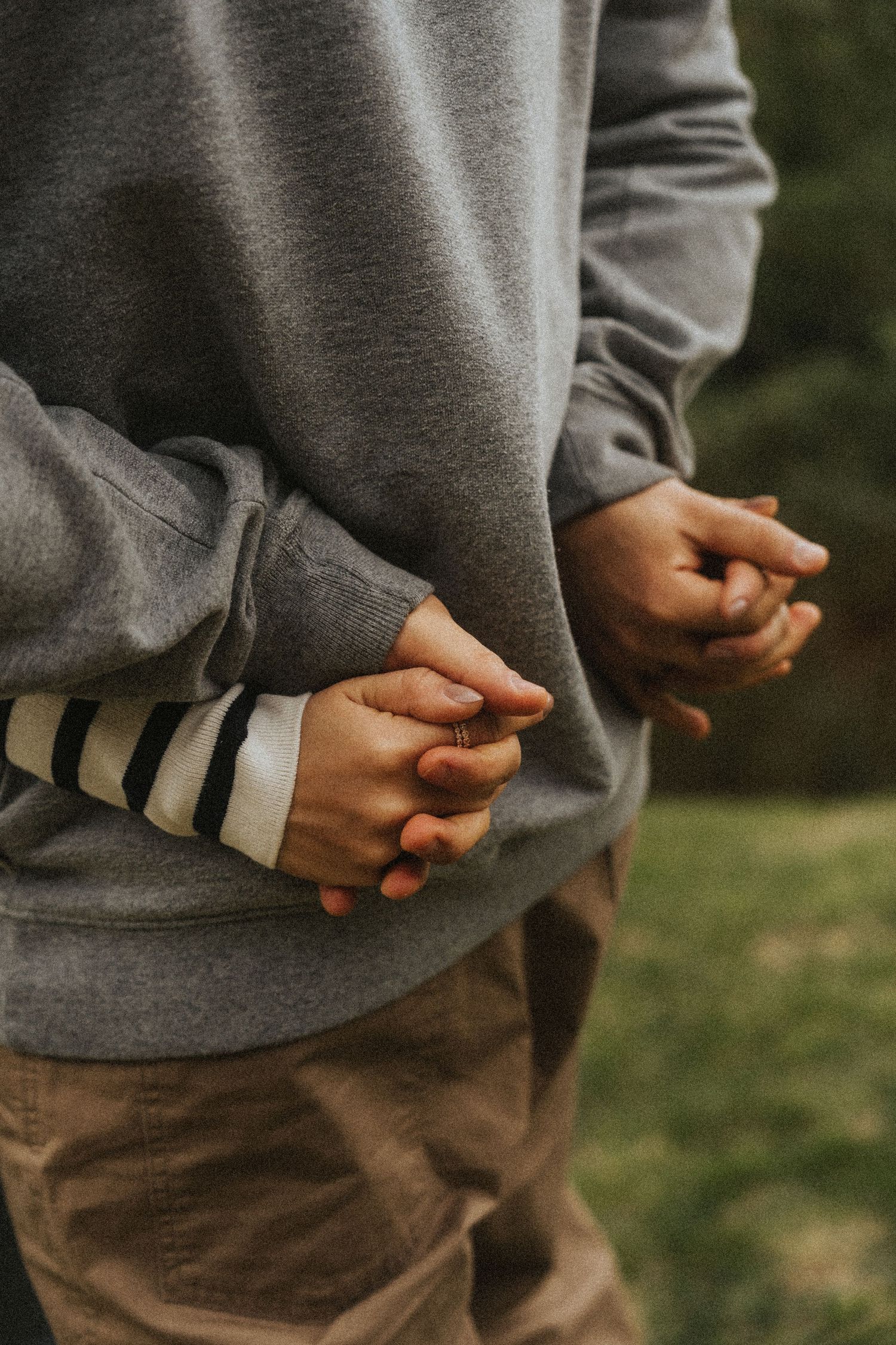 Close-up series of hands in gray sleeves holding something small while standing outdoors in nature.