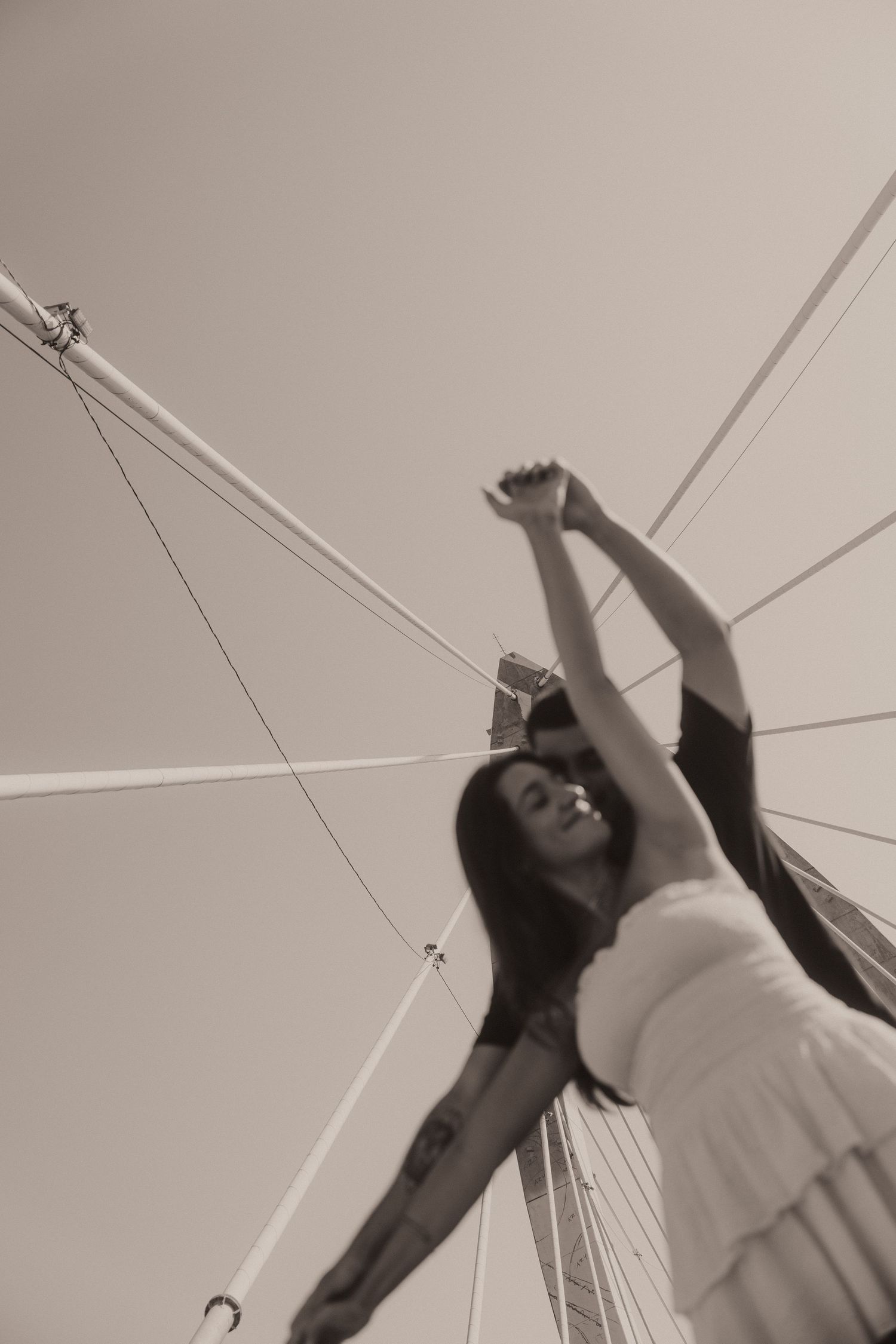 Artistic low angle view of a dancing couple captured through geometric suspension bridge lines.