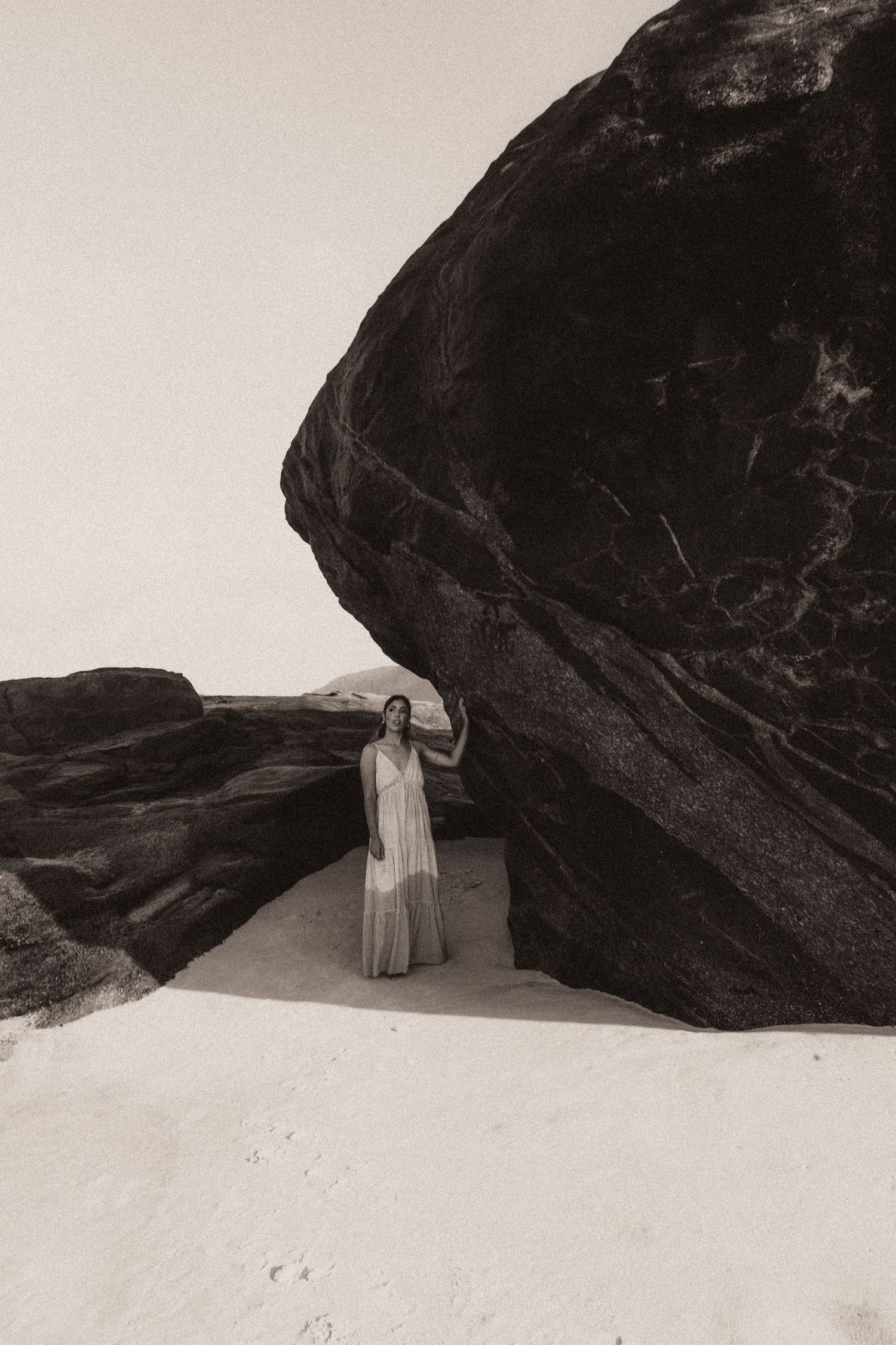 Figure in white dress stands against dramatic black rock formations in black and white landscape photography series.