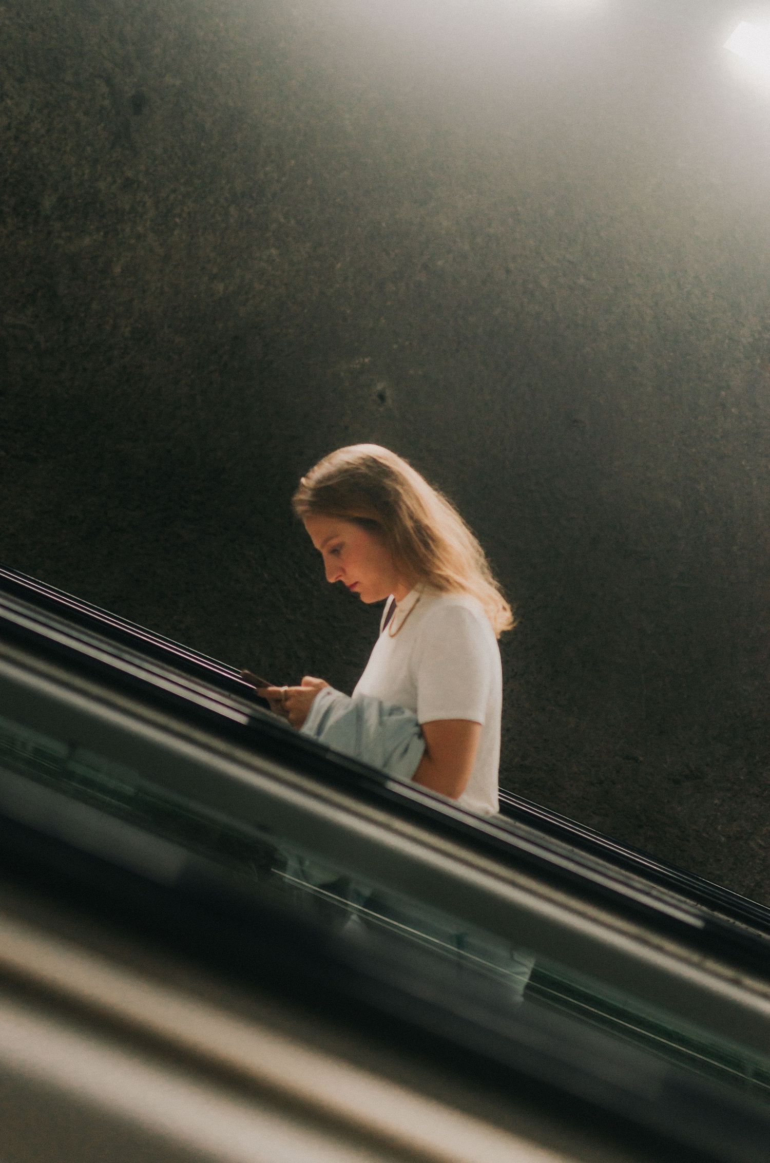 Side view of someone checking their phone while going up an escalator in dark lighting.