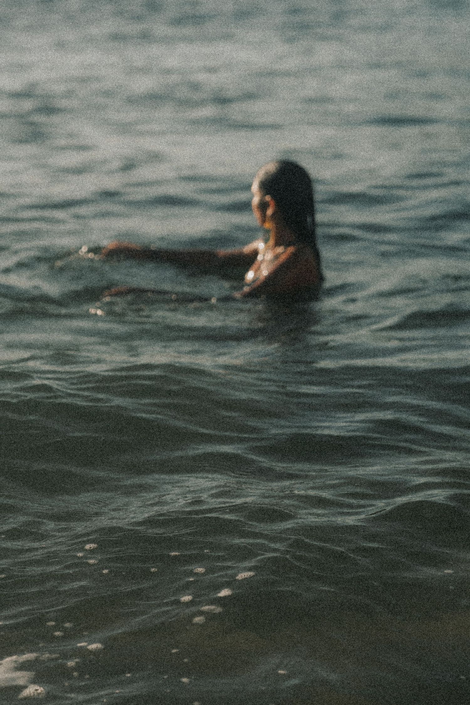 A figure emerges from dark moody waters while swimming in a tranquil ocean scene.