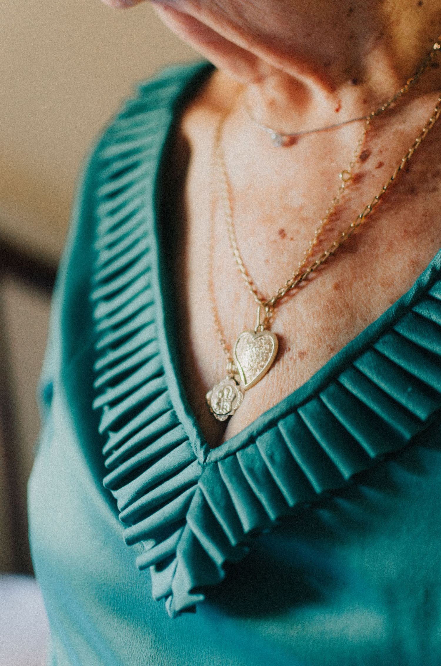 Close-up view of a turquoise ruffled neckline with a delicate heart pendant necklace.
