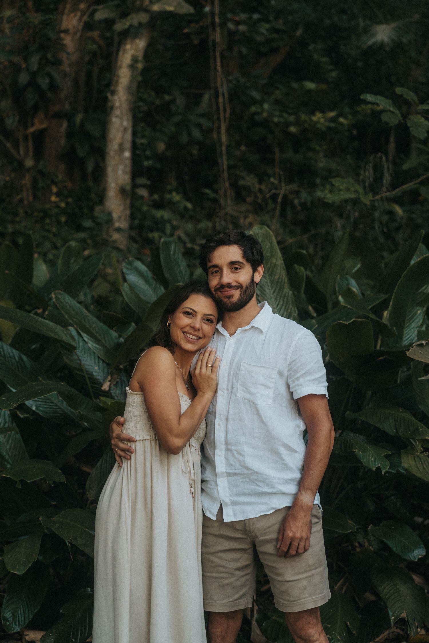 A couple shares intimate moments in a lush tropical garden setting wearing light summer attire and embracing.