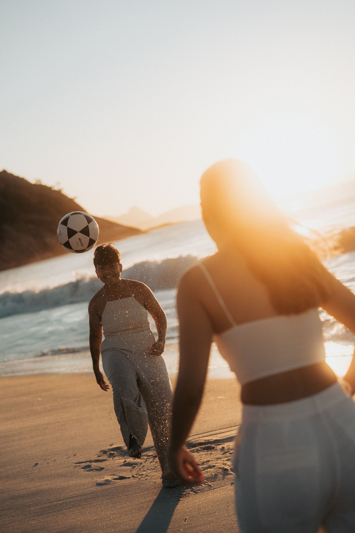 Two silhouetted figures enjoy a golden sunset on a sandy beach as waves roll in along the shore.