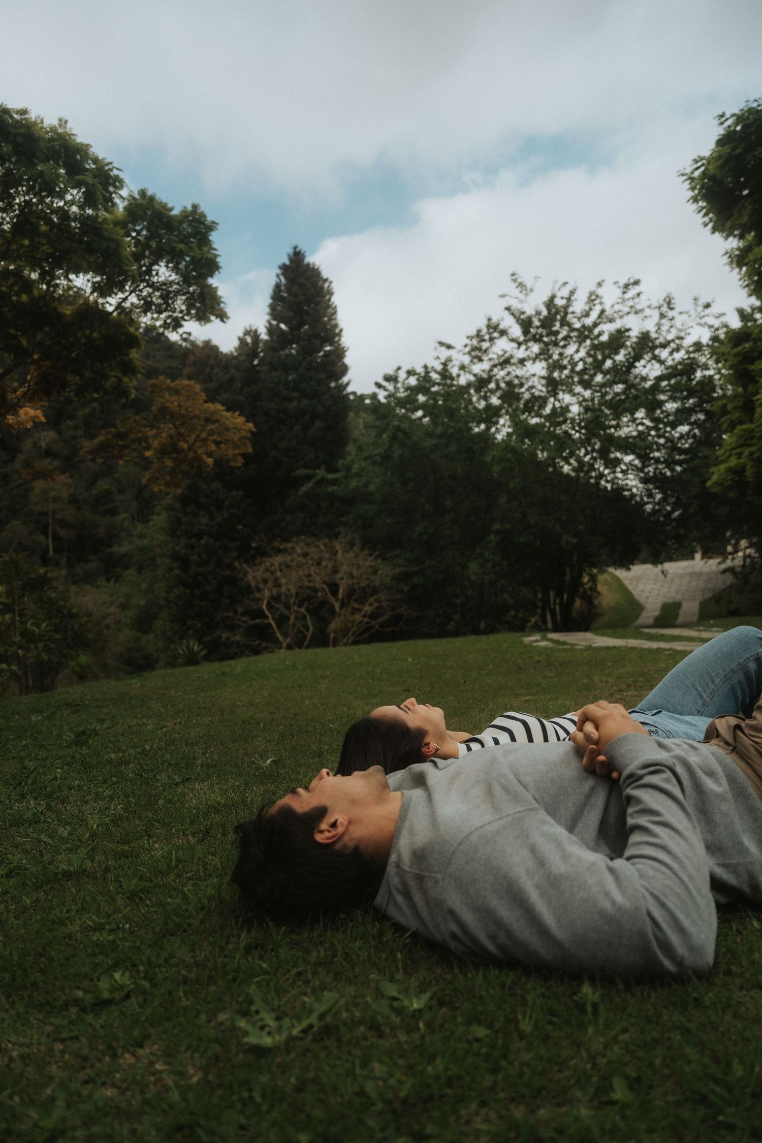 A person lies peacefully on a grassy hillside under cloudy skies on an autumn day.