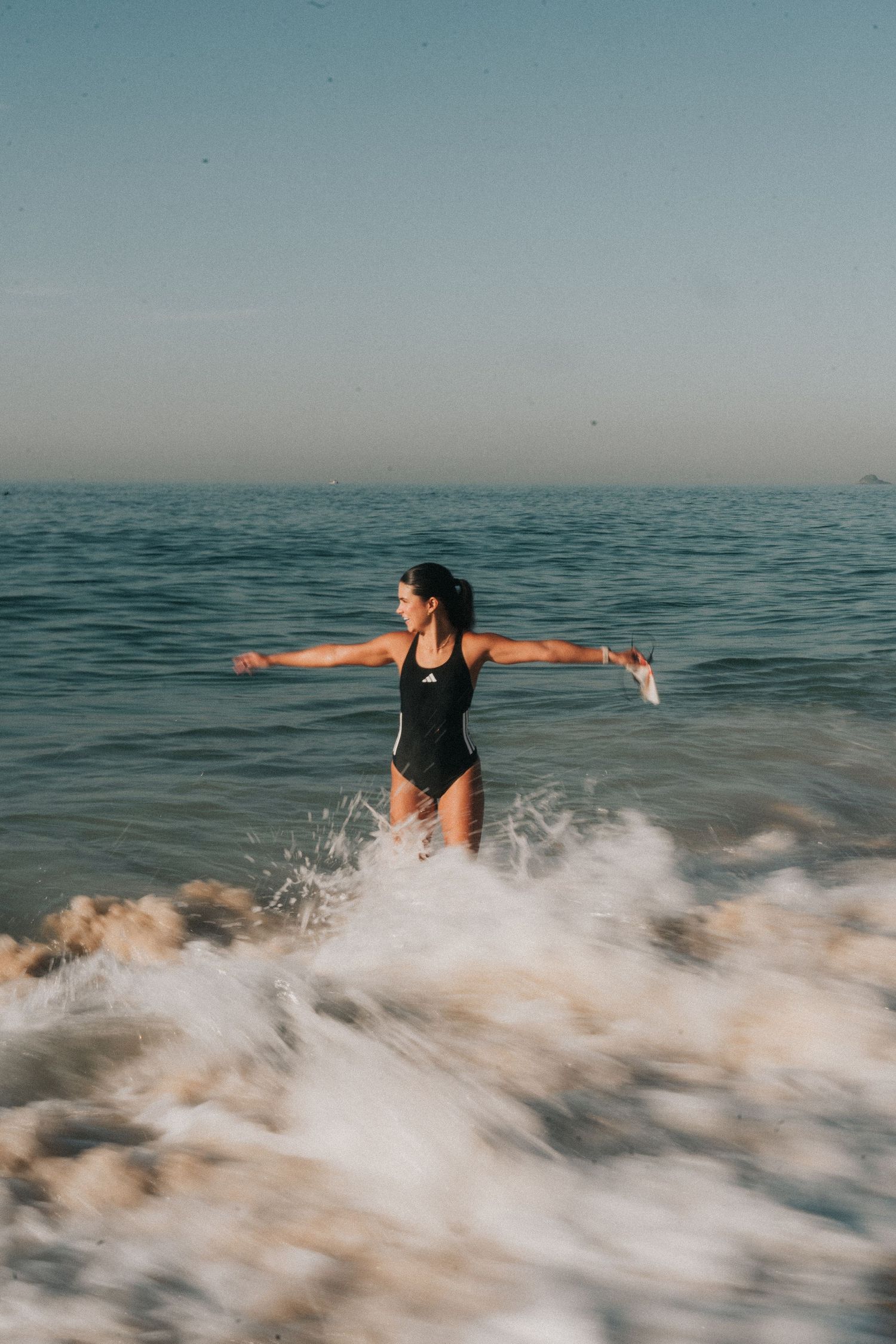 Person in black swimsuit splashing through ocean waves during golden hour, creating dynamic water motion.