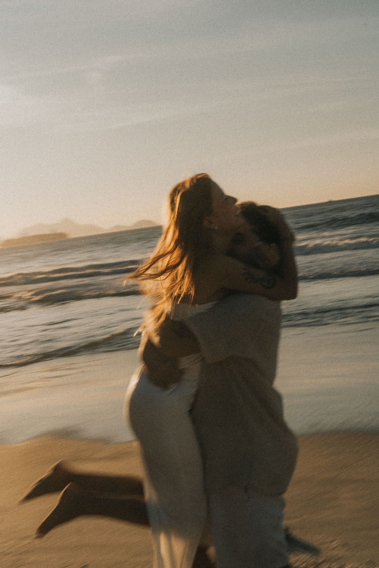 Dancing couple embraces on misty beach at sunset, creating romantic silhouettes against the ocean waves.