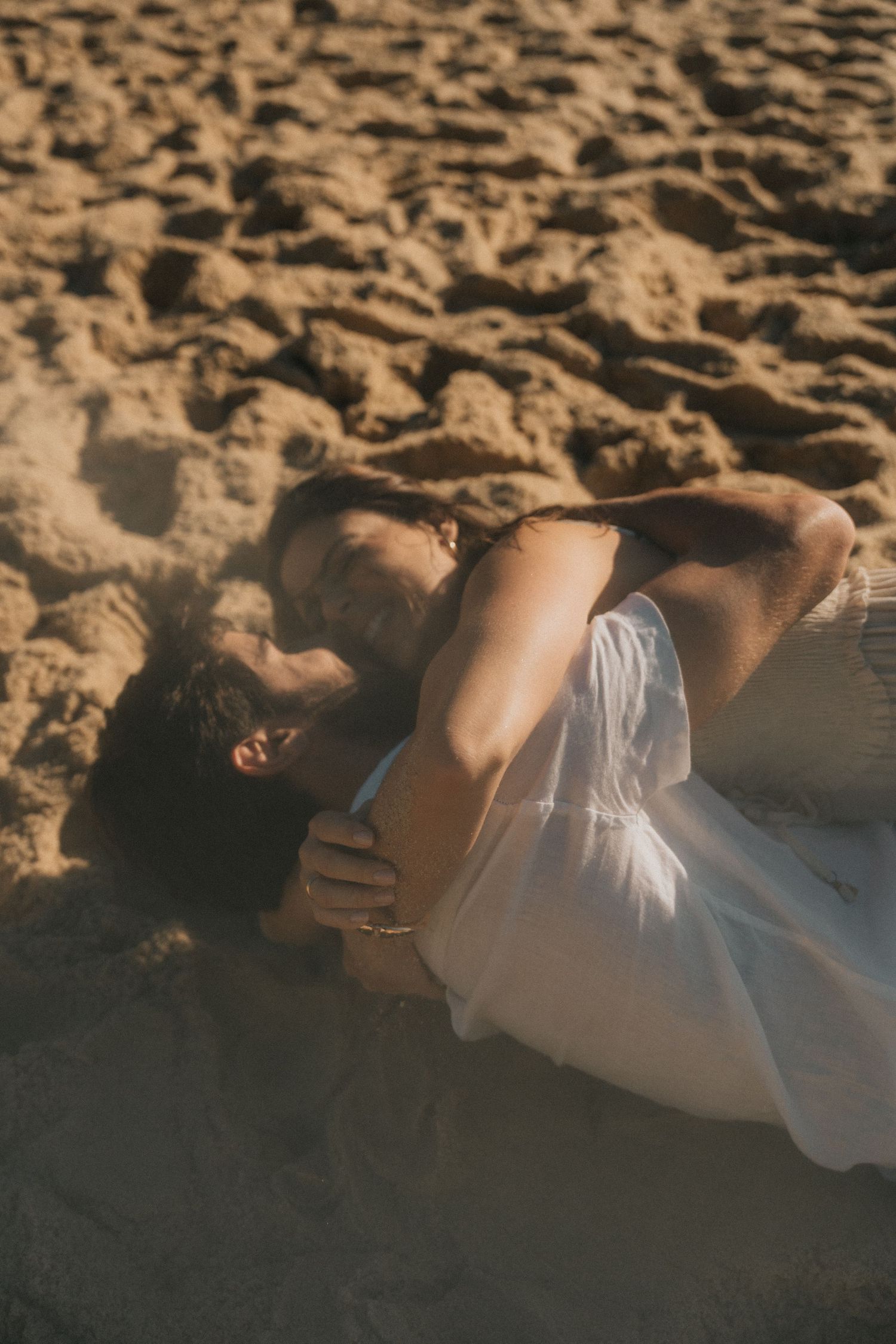Person in white dress lying on textured sand at the beach during sunset creating an artistic silhouette.