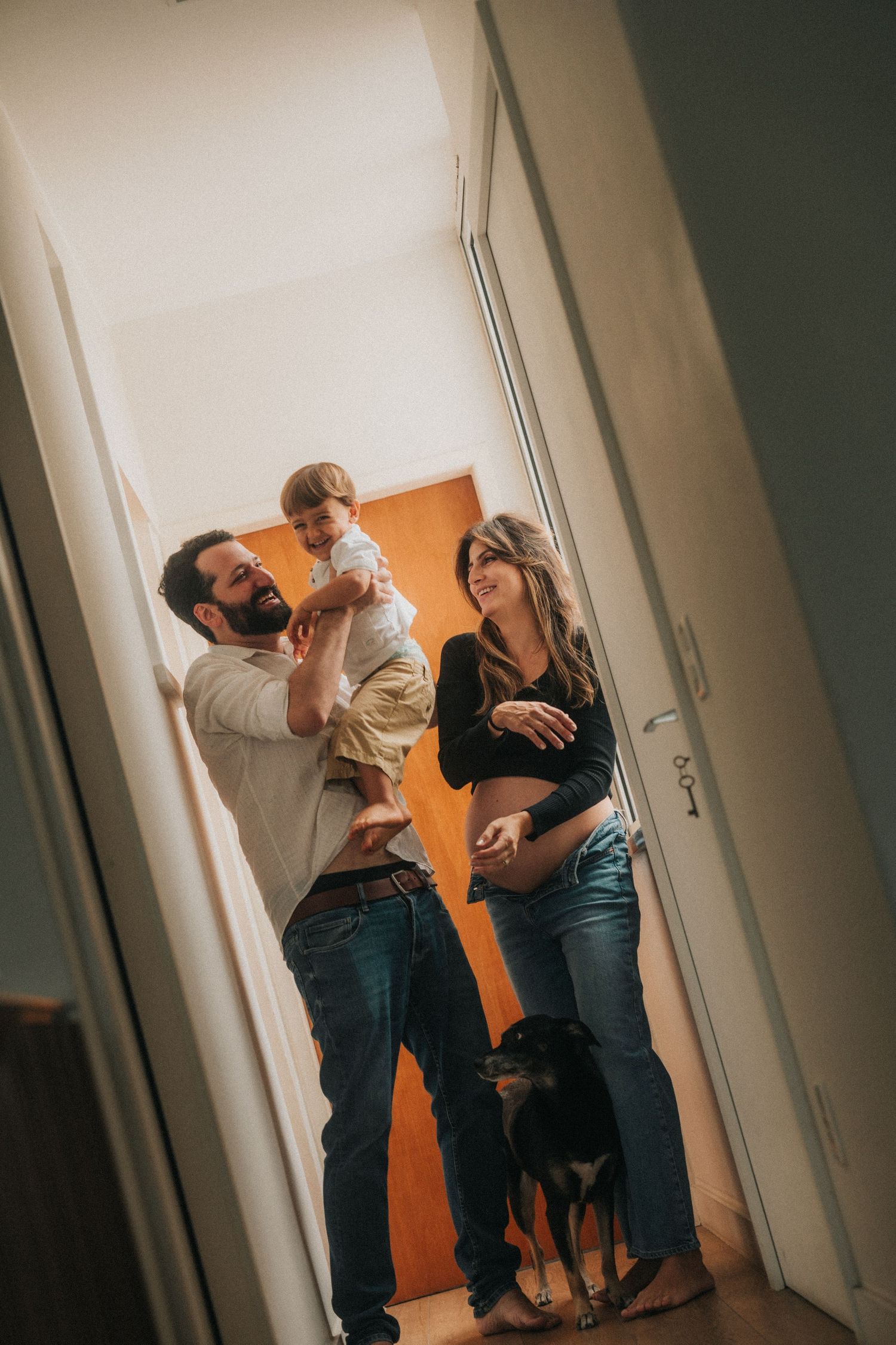 A family moment in a hallway with a baby and dog, captured in warm lighting.