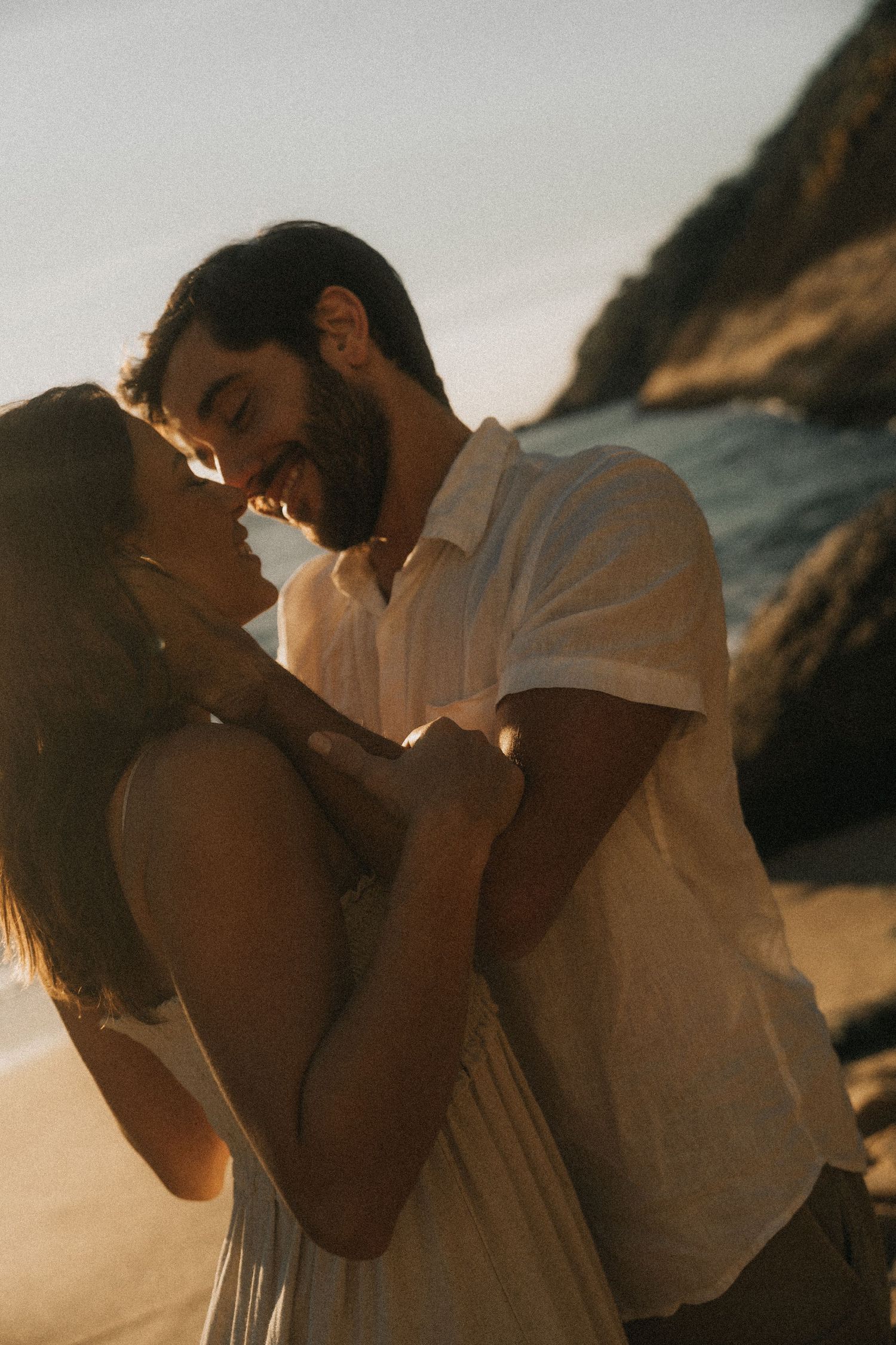 Romantic silhouettes of a couple embracing at sunset near a rocky beach.