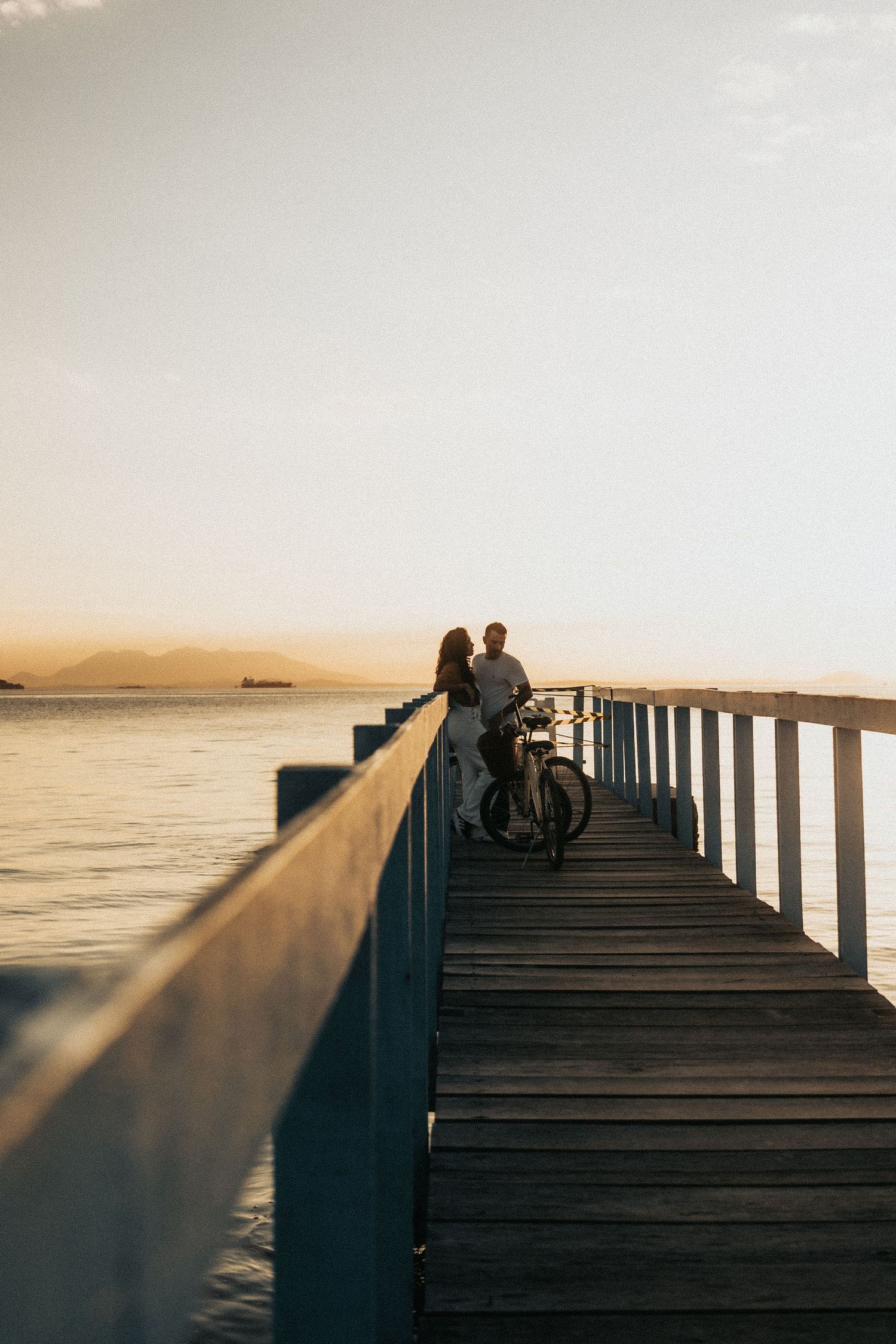 A series of silhouettes sitting on a wooden pier at sunset, creating a peaceful coastal scene along the ocean horizon.