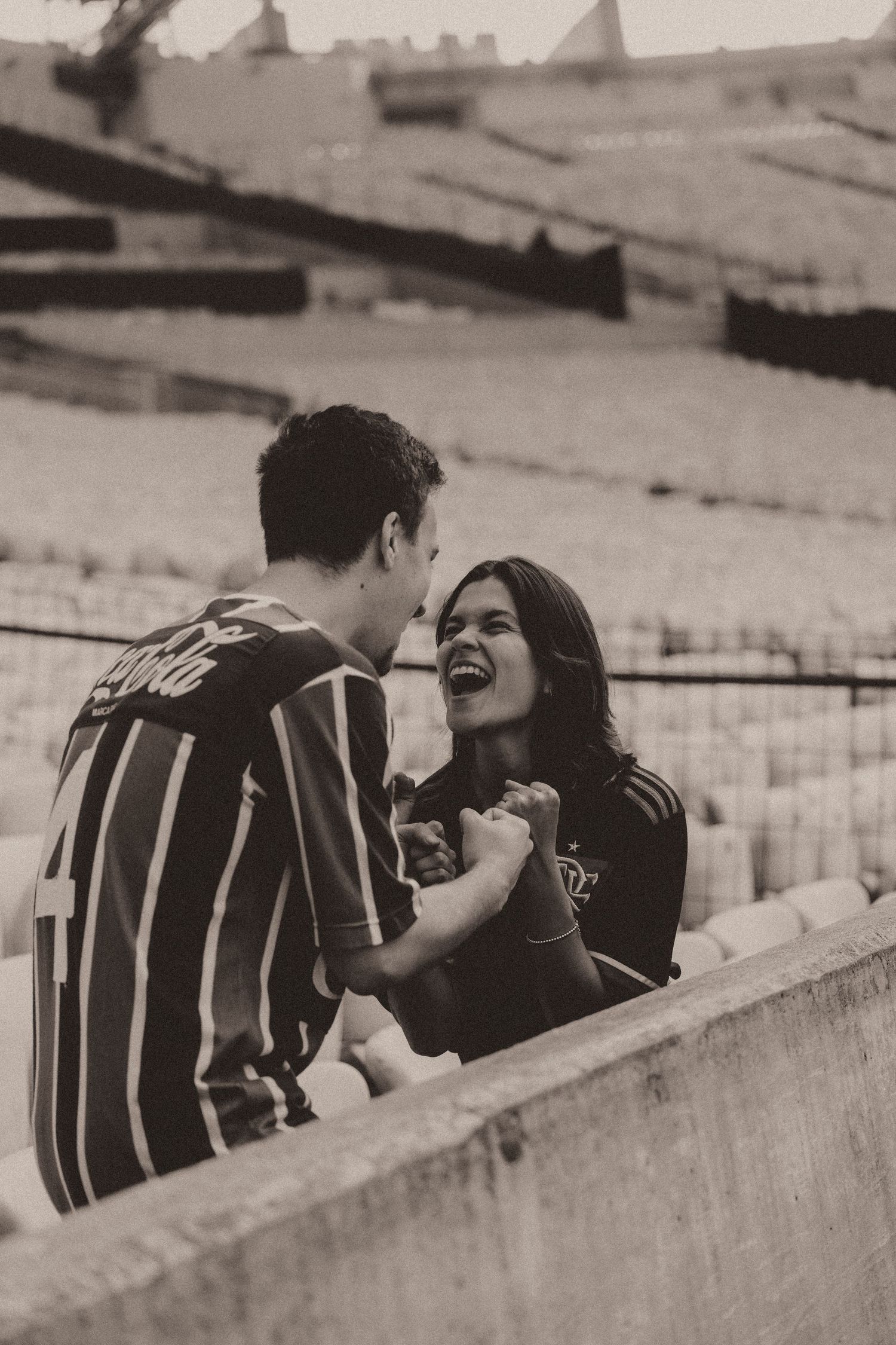 Black and white sequence showing a couple expressing joy and laughter while sitting in an empty stadium.