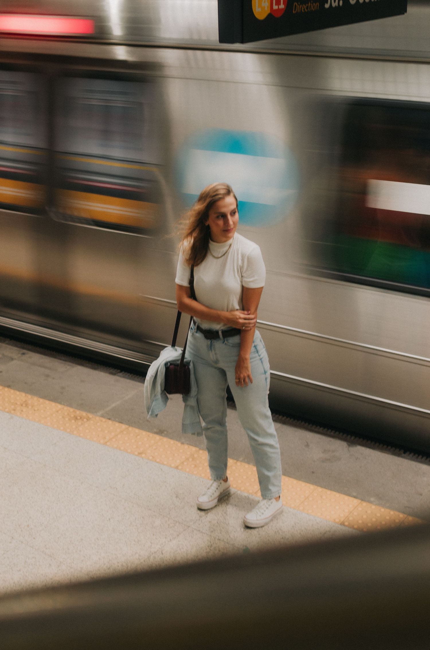A person stands at a subway platform with motion-blurred trains creating a dynamic urban transit scene.