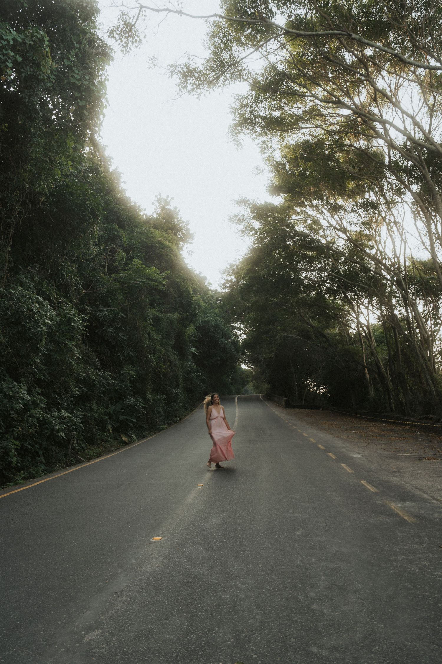 People riding longboards down a winding tree-lined road on a cloudy day.