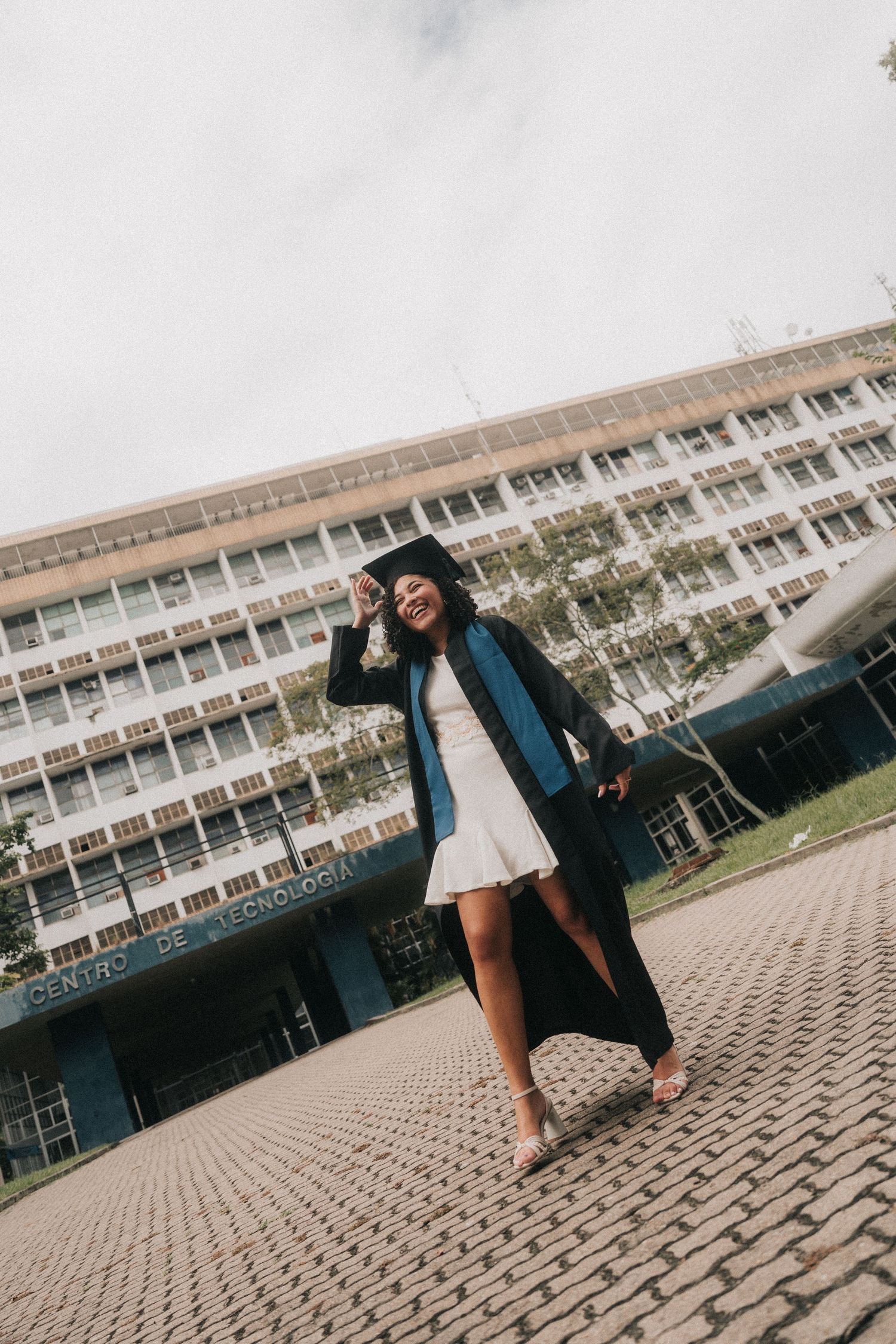 People in graduation attire celebrate and pose on a geometric patterned courtyard in front of a modern building.