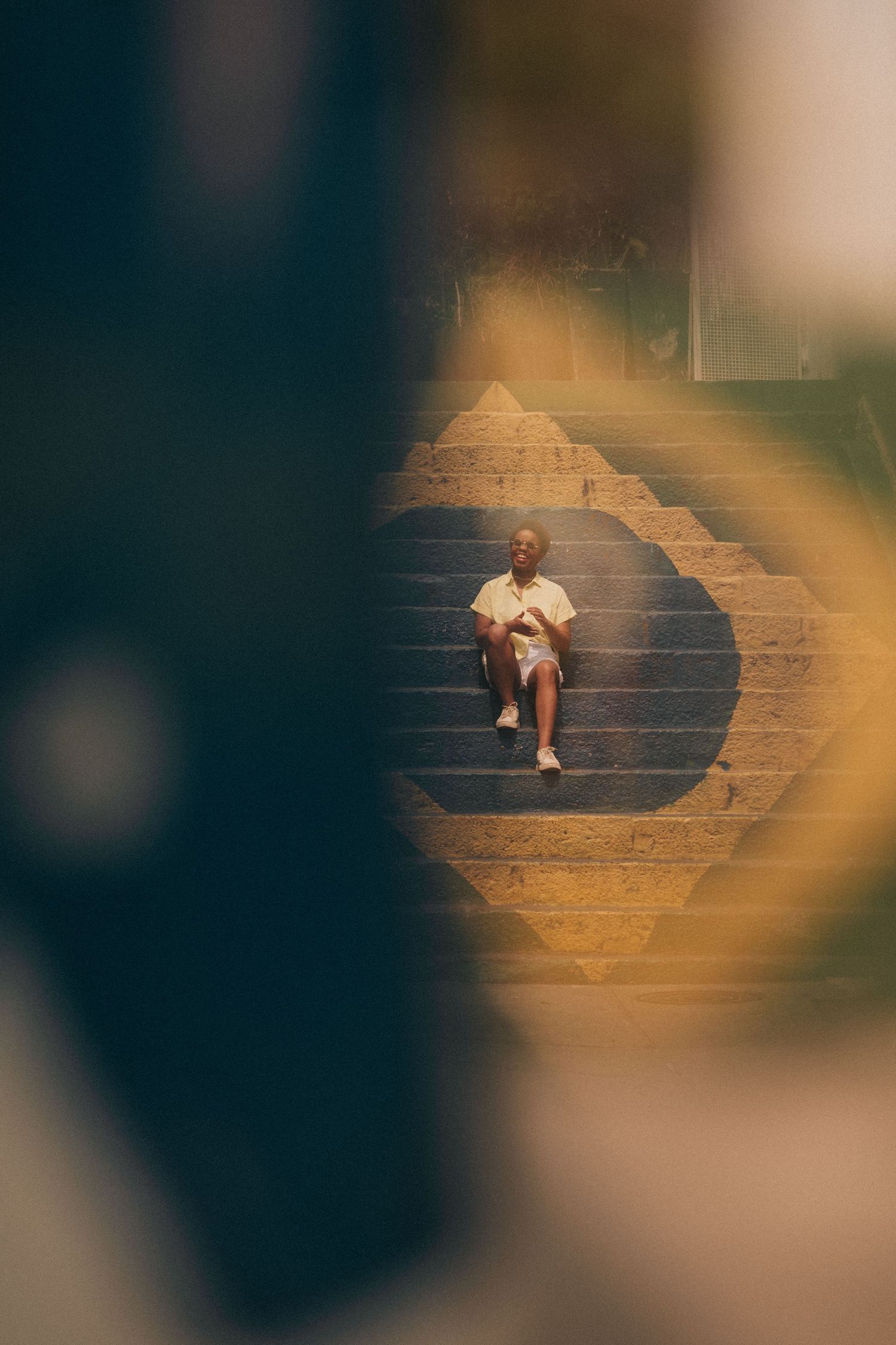 Person wearing white shirt sits alone on light-colored stone steps in a dreamy, golden-lit setting.