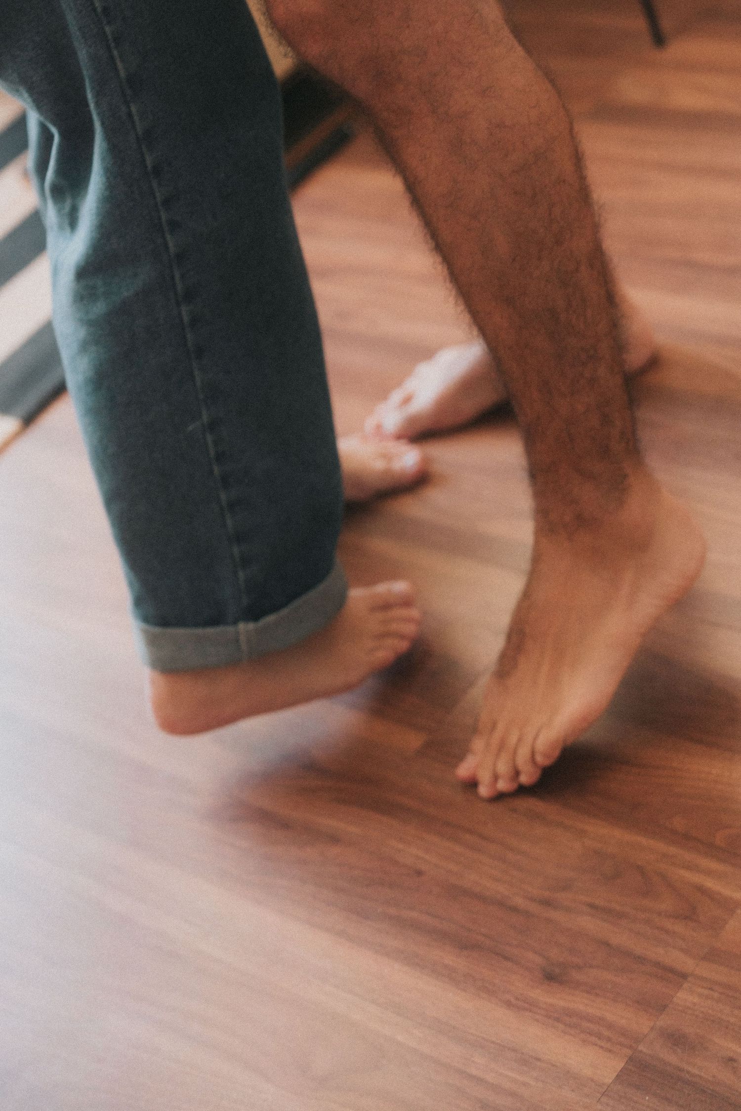 Sequence of bare feet and blue jeans stepping on hardwood floor showing movement across wooden planks.