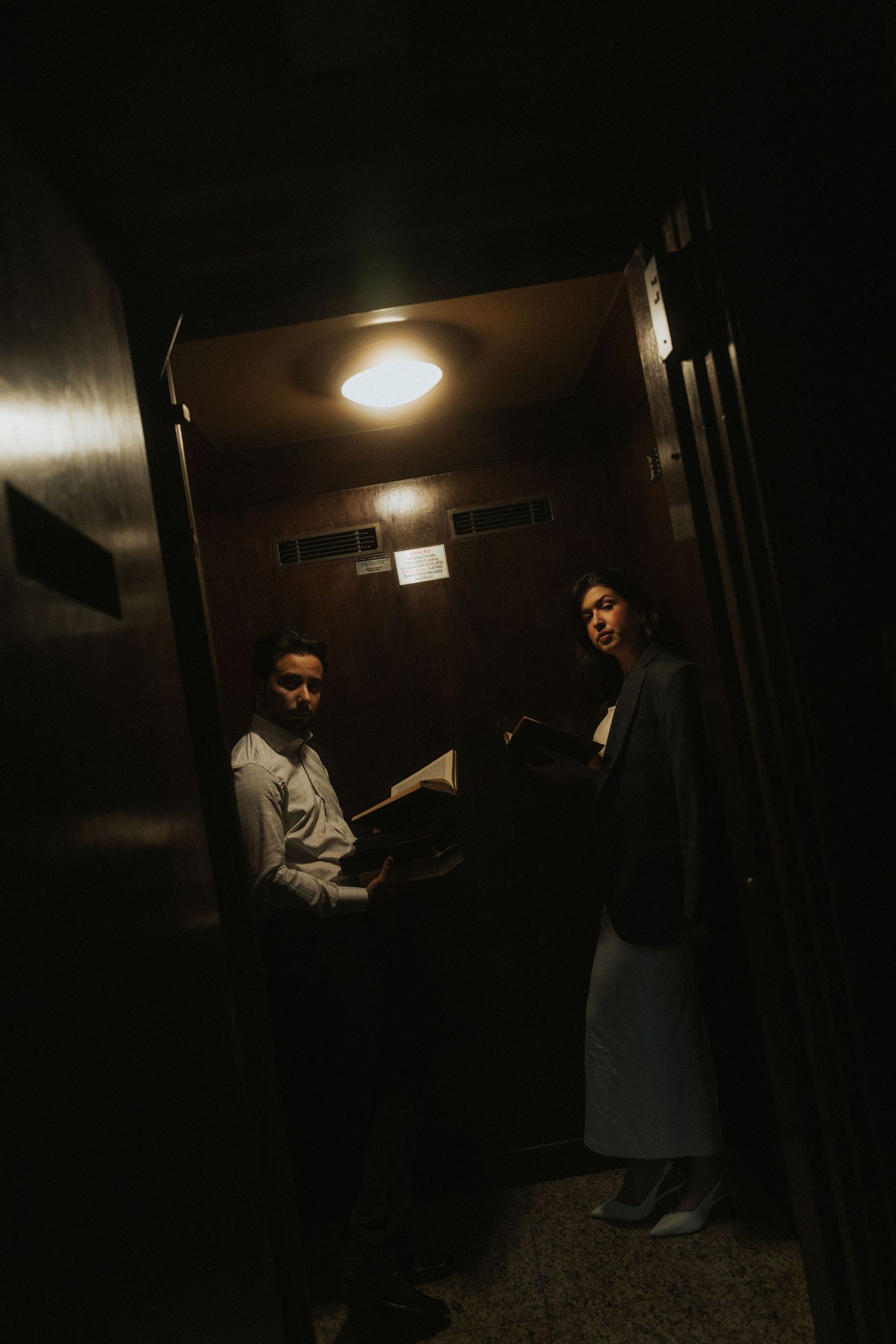 A dimly lit hallway with figures moving through shadows and overhead lighting creating an eerie atmosphere.