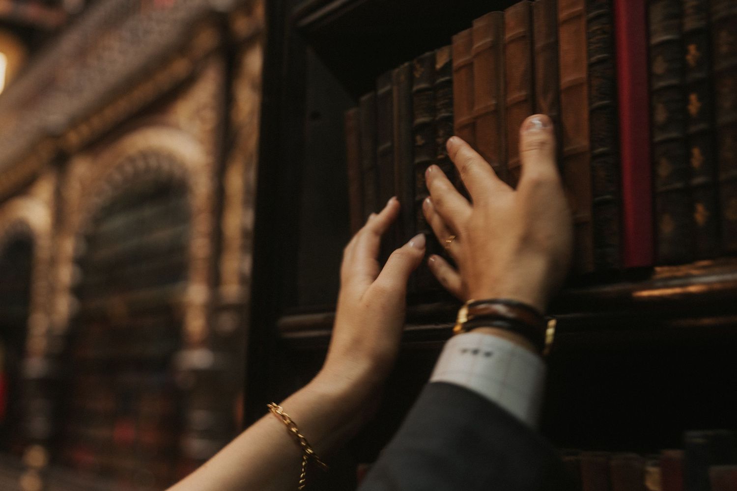A person's hand reaches up to touch books on a wooden bookshelf in a dimly lit library.