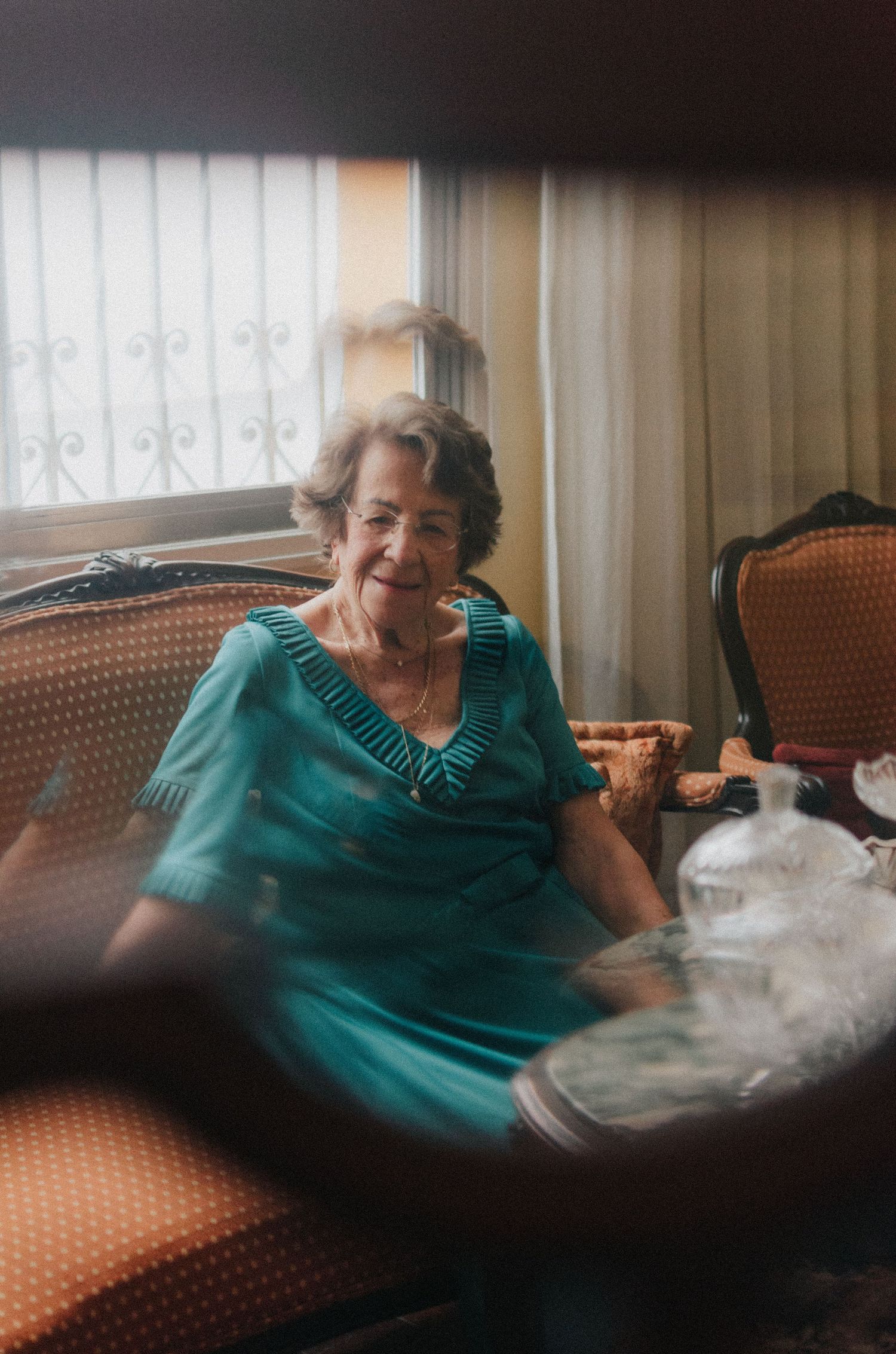 A person in a teal dress sits on a vintage sofa in soft lighting creating a nostalgic atmosphere.