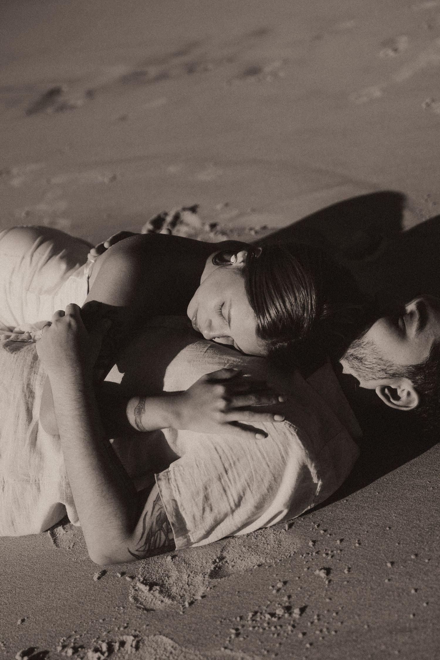 A sequence of black and white artistic photographs showing a figure in dramatic reclining poses on a sandy surface.