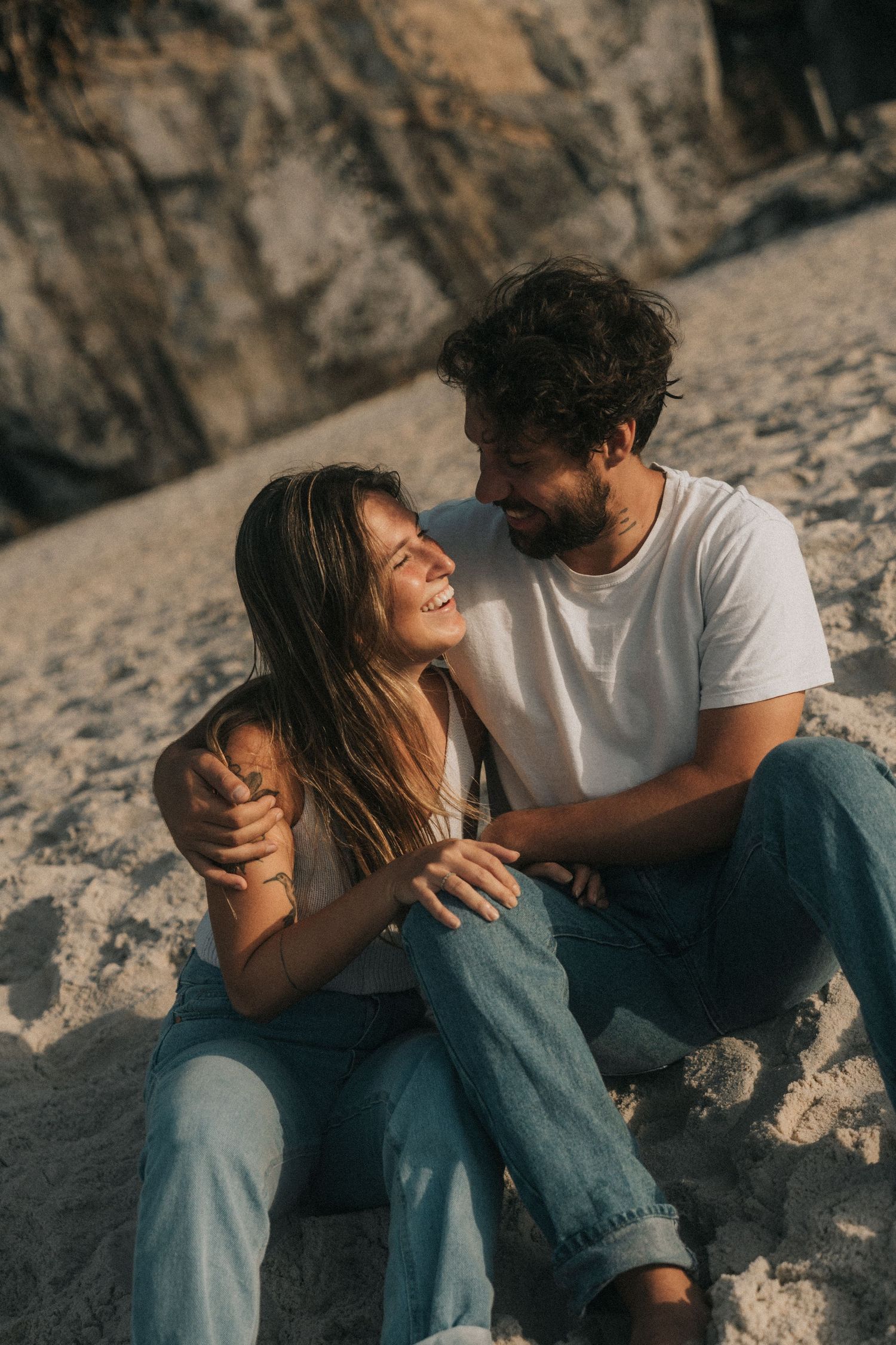 A couple sits together on sandy rocks sharing intimate moments through a series of romantic candid photos.