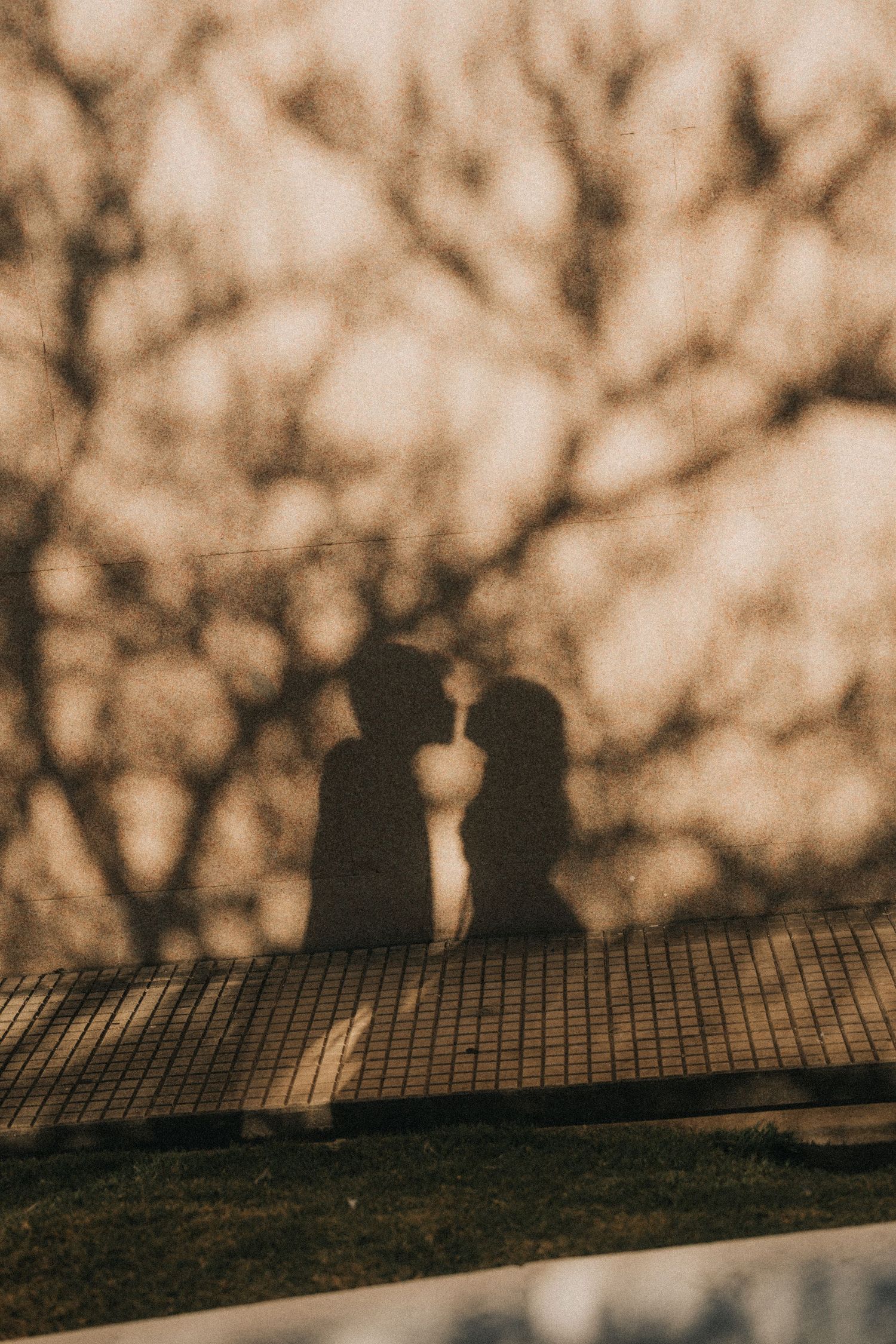 Two silhouettes sit close together on a railing against a blurred bokeh background at sunset.