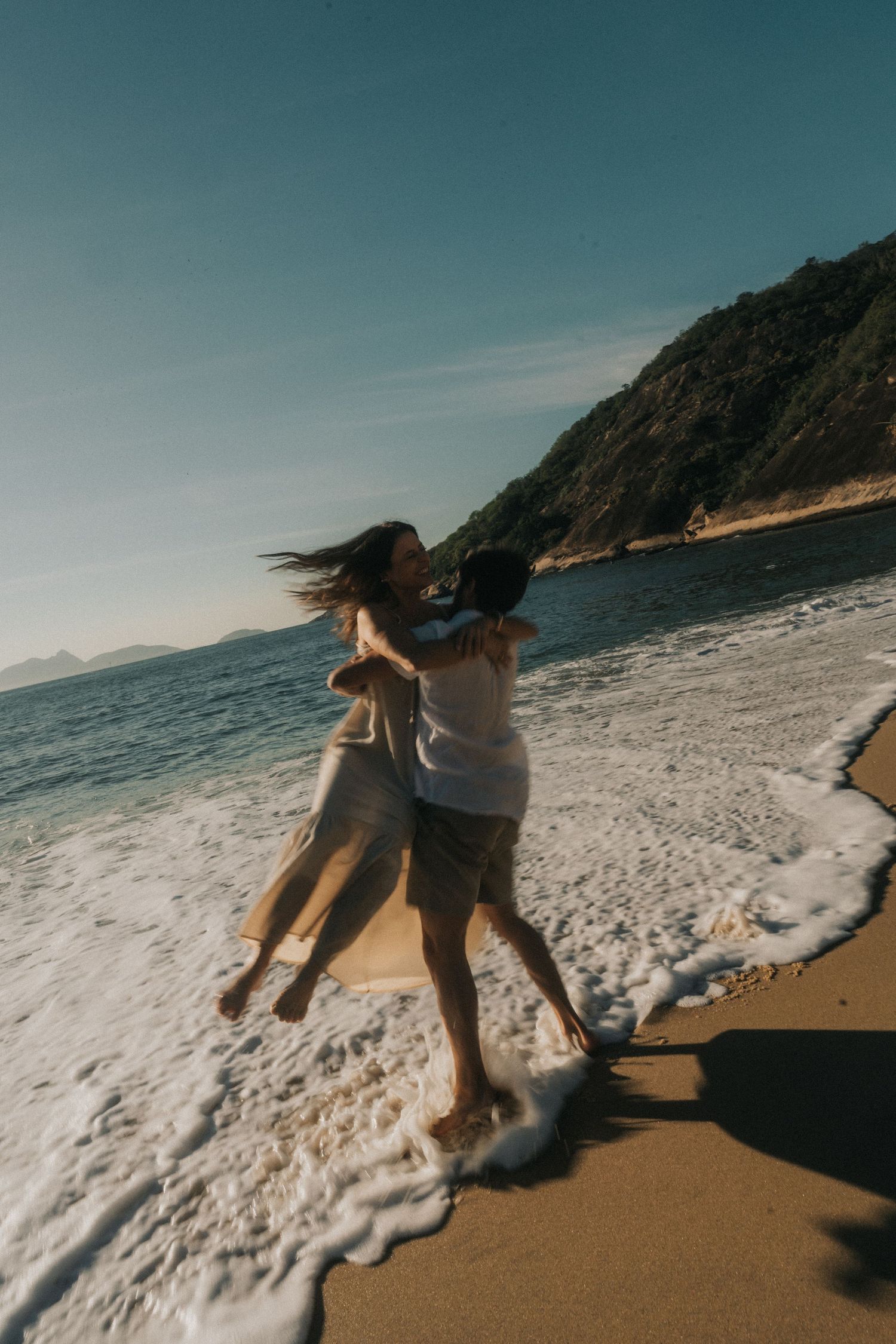Two people playfully running and dodging ocean waves together on a scenic sandy beach during golden hour.