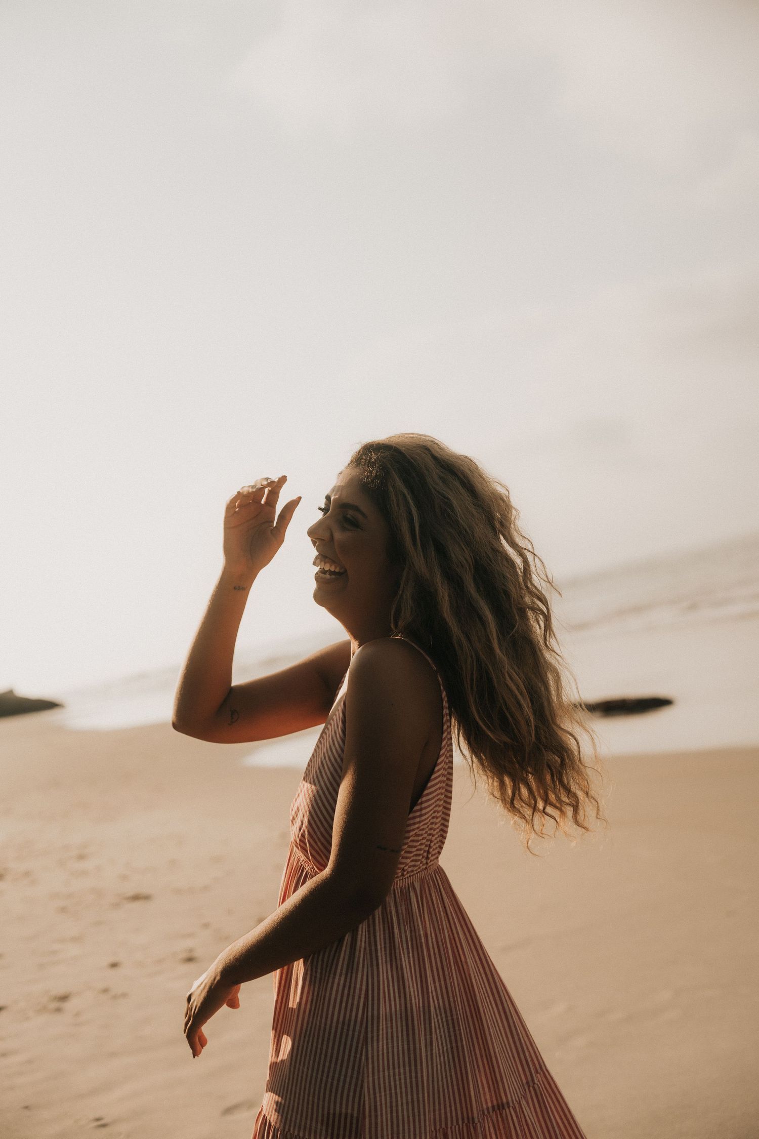 A person in a striped dress dances elegantly on sand dunes at sunset, creating a dreamy silhouette against the sky.