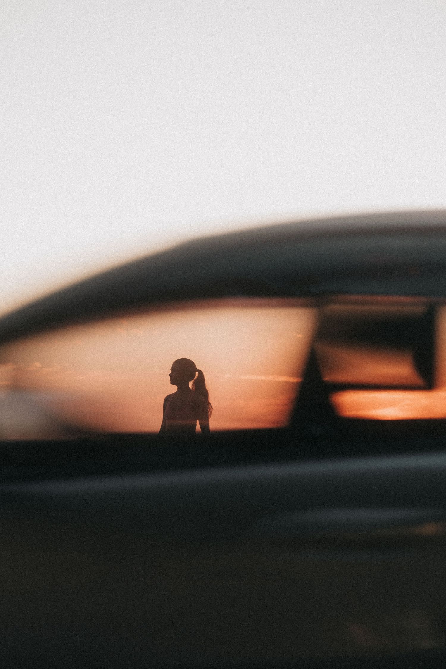 Silhouette figure viewed through car window against vibrant orange sunset sky in artistic blur photography.