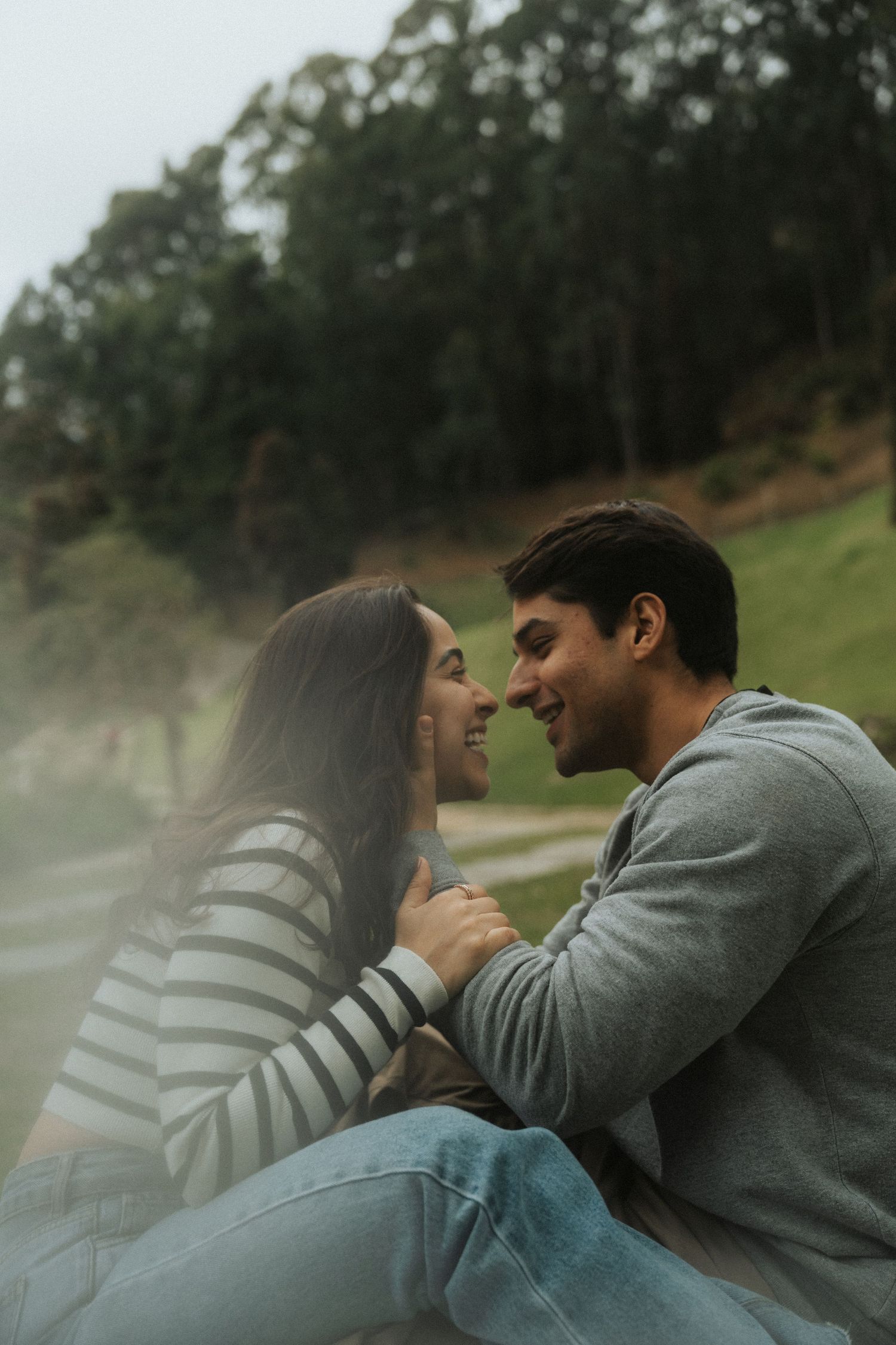 A couple shares an intimate moment together on a misty hillside in matching gray and striped sweaters.