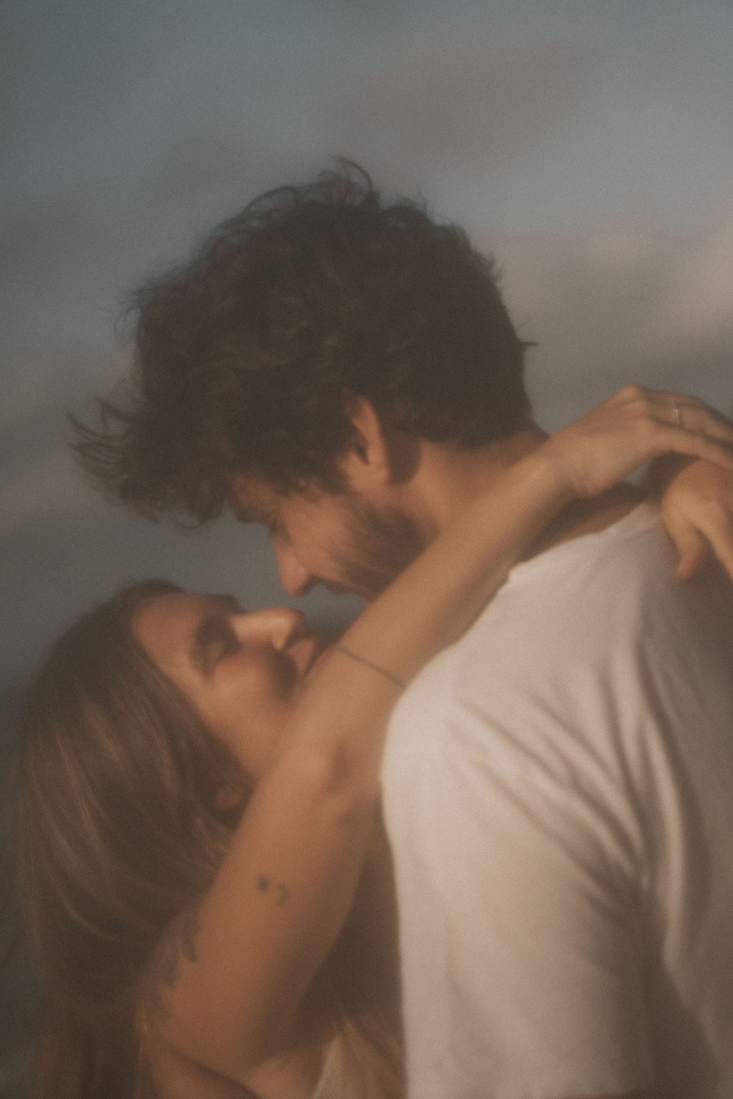 Casal em momento íntimo, luz suave e céu dramático — cena de filme apaixonado no Rio de Janeiro.