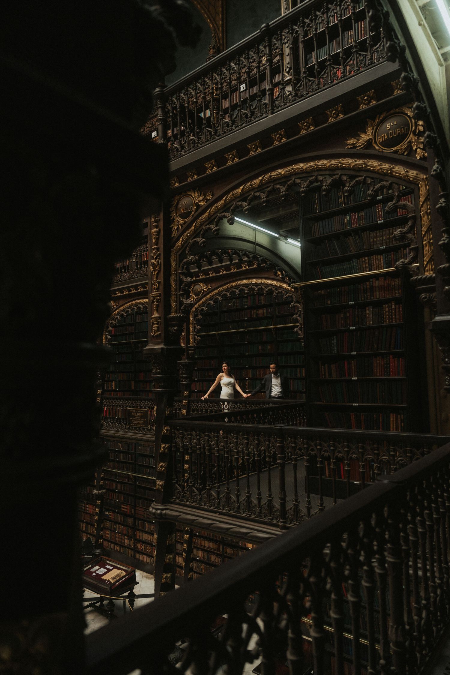 A series of ornate wooden spiral staircases in a historic library with dark wooden bookshelves and intricate carvings.