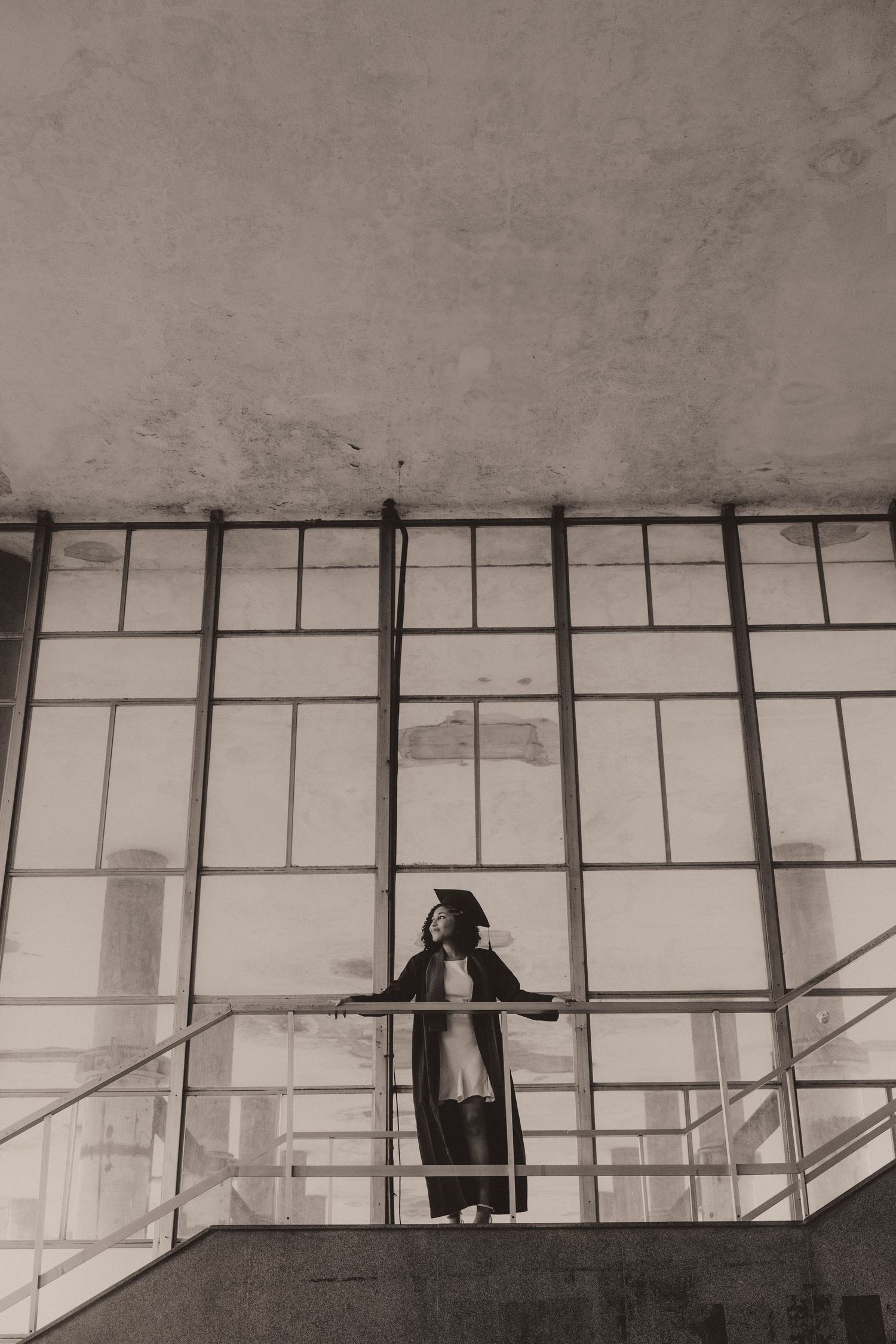 A dark silhouette of a person on a balcony with geometric glass panels creates a minimalist architectural composition.