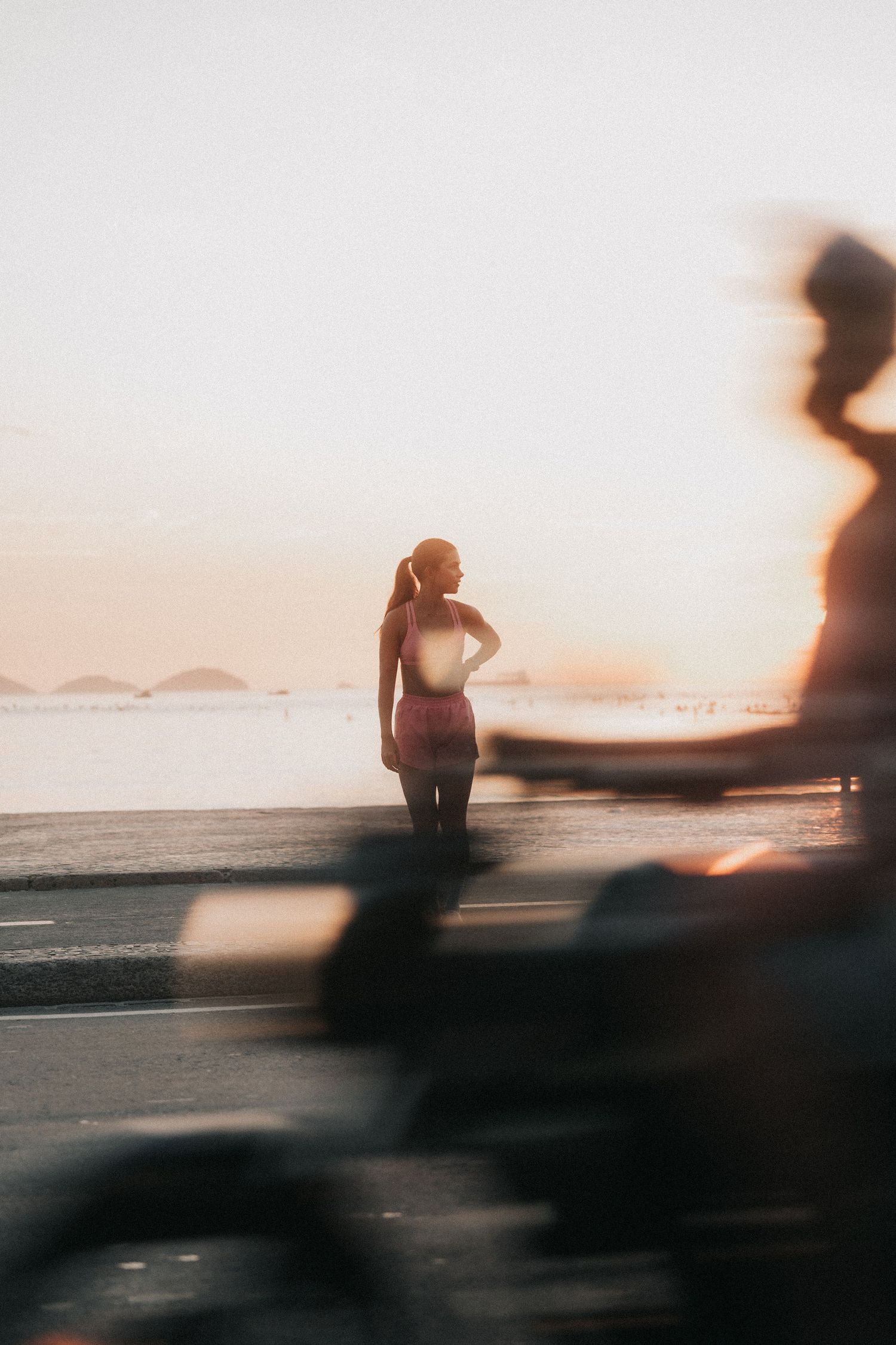 Silhouetted figure stands on beach at sunset with motion blur in foreground creating dreamy atmosphere.