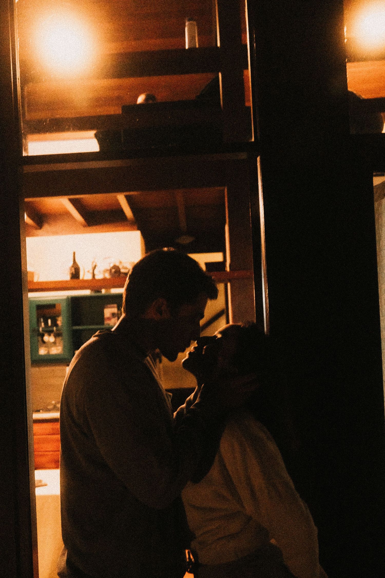 Silhouettes of people sit at a dimly lit bar counter with warm ambient lighting creating a moody atmosphere.