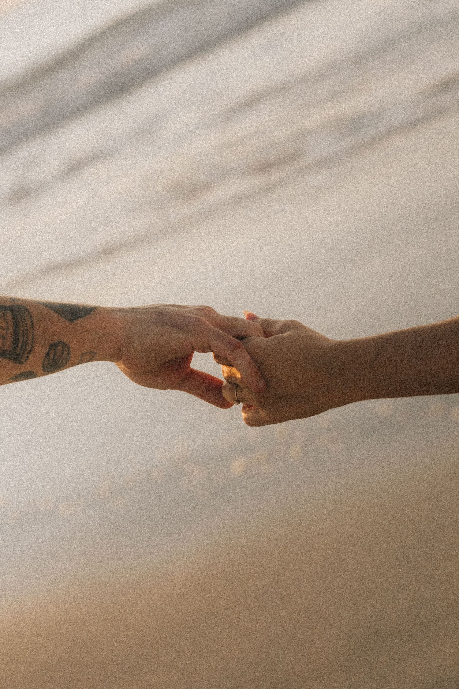 Two arms meeting in ethereal embrace against a soft beige background create a minimalist artistic composition.