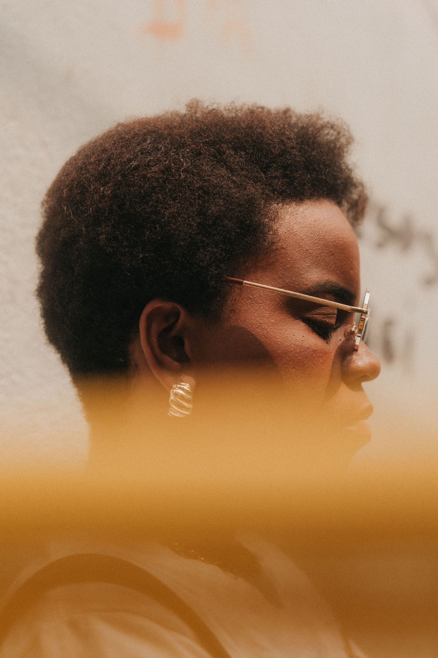 Artistic profile silhouette of a person with afro hair and glasses against warm orange atmospheric lighting.
