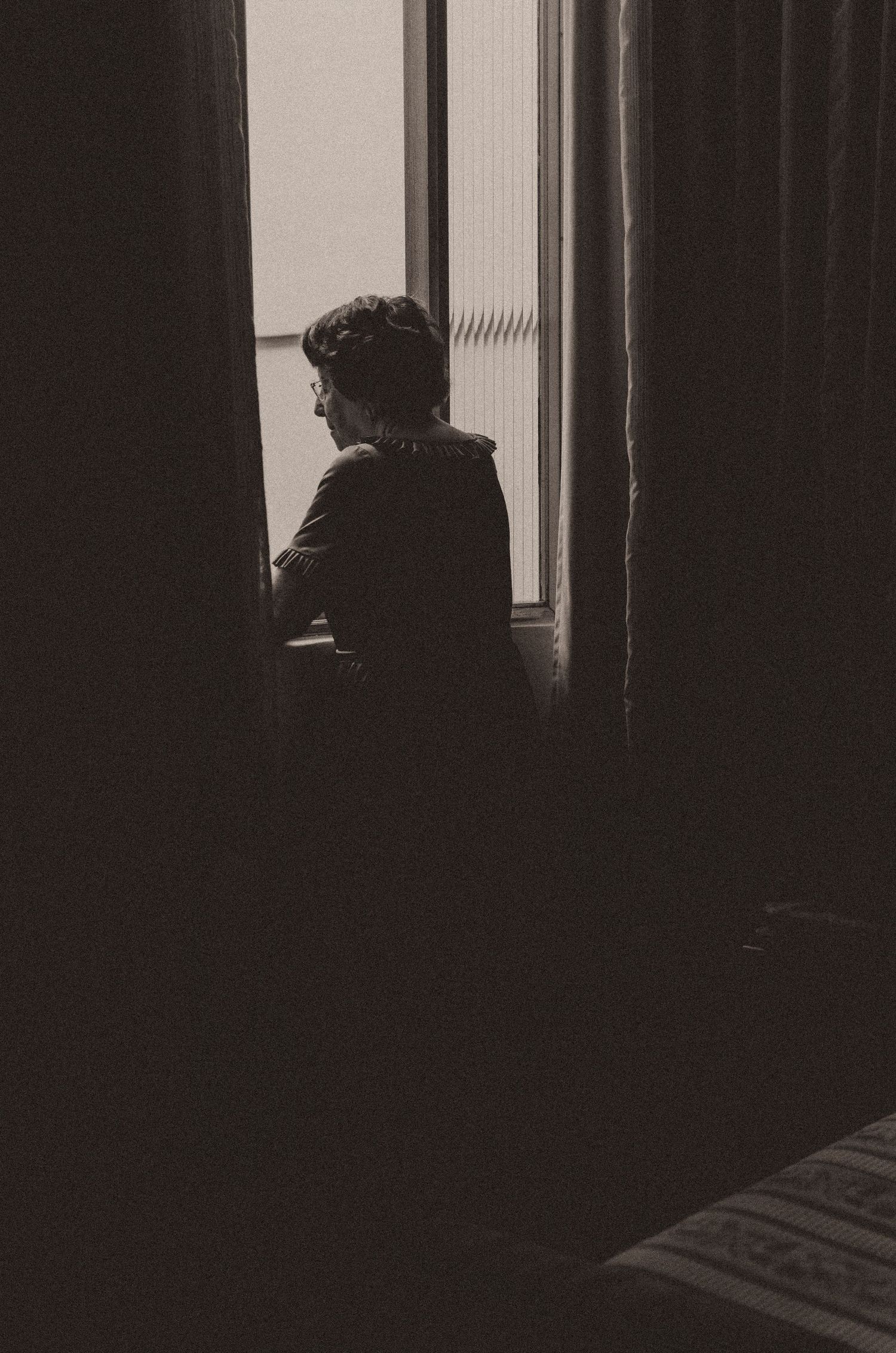 A dark and moody silhouette of a person standing by a window in a dimly lit interior space.
