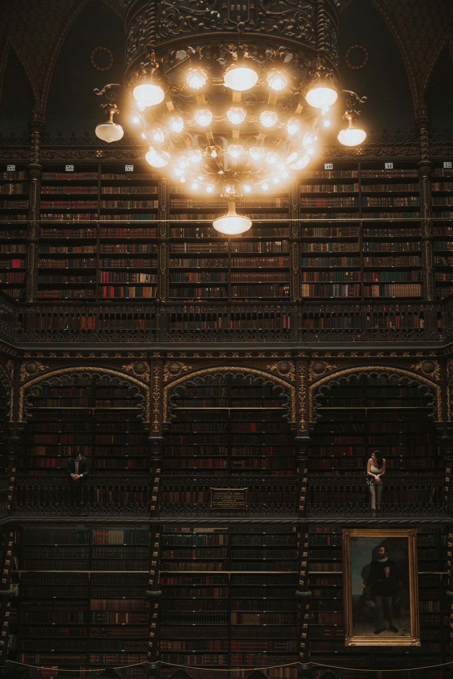 Ornate vintage library interior with dark wooden bookshelves, elaborate ceiling details, and warm glowing light fixtures.
