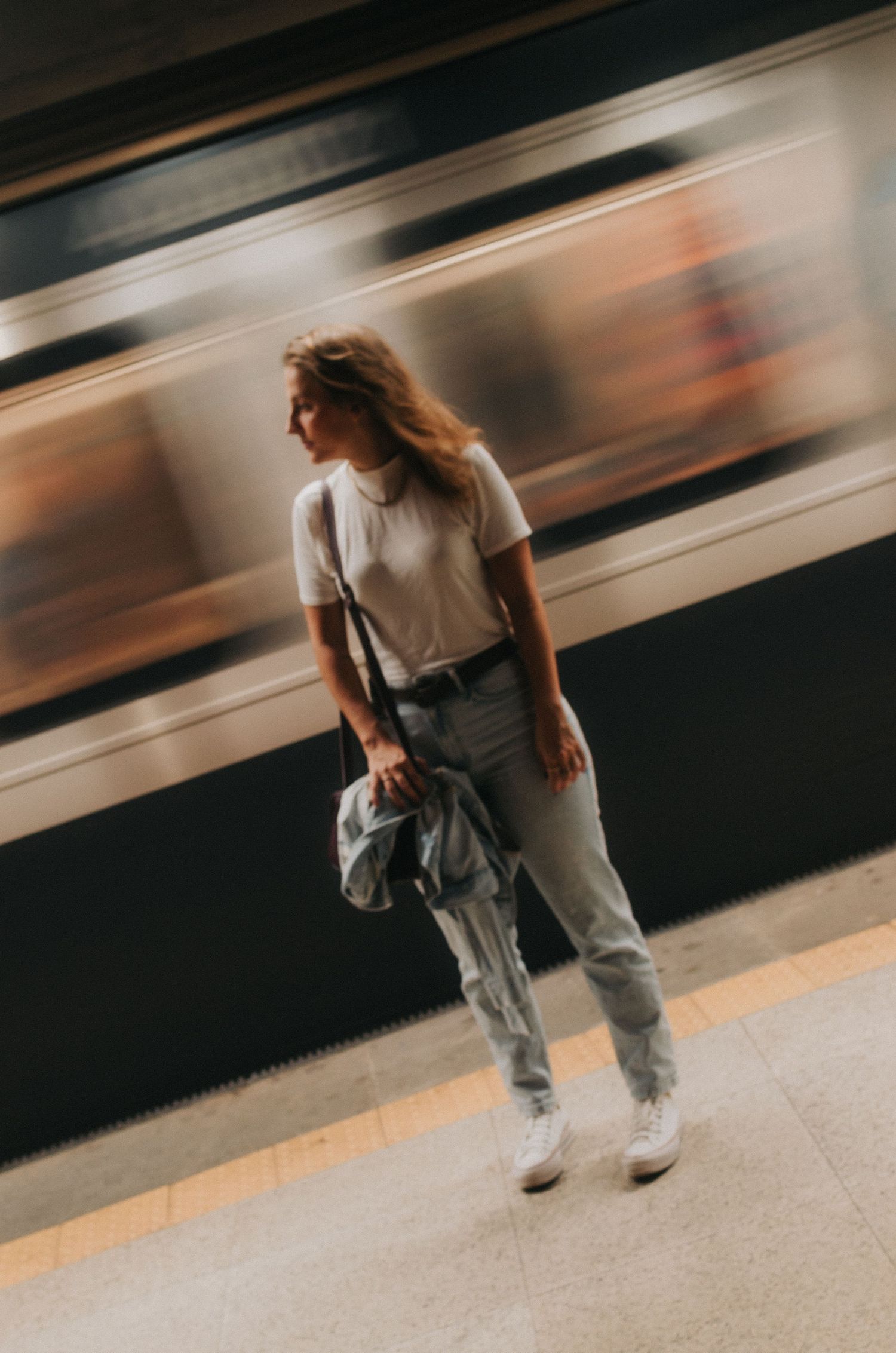 Motion blur captures person sitting on subway platform with train passing by in long exposure photography.