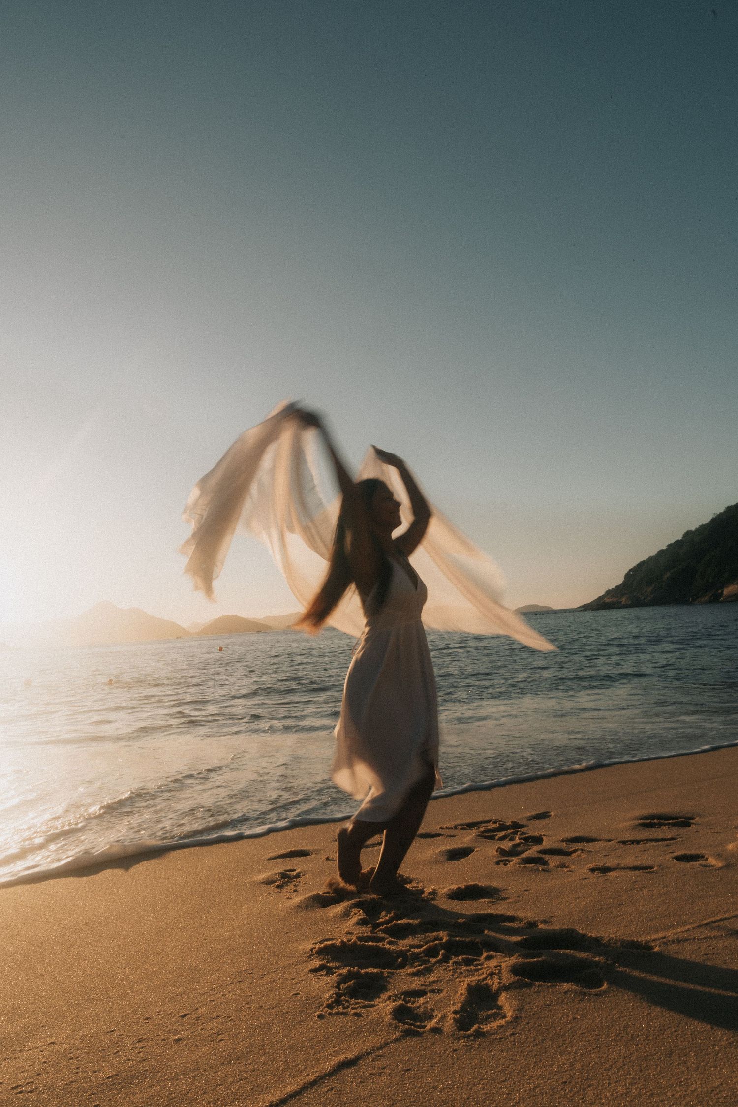 A silhouette dances gracefully on a beach at sunset, creating movement with flowing fabric against the ocean backdrop.