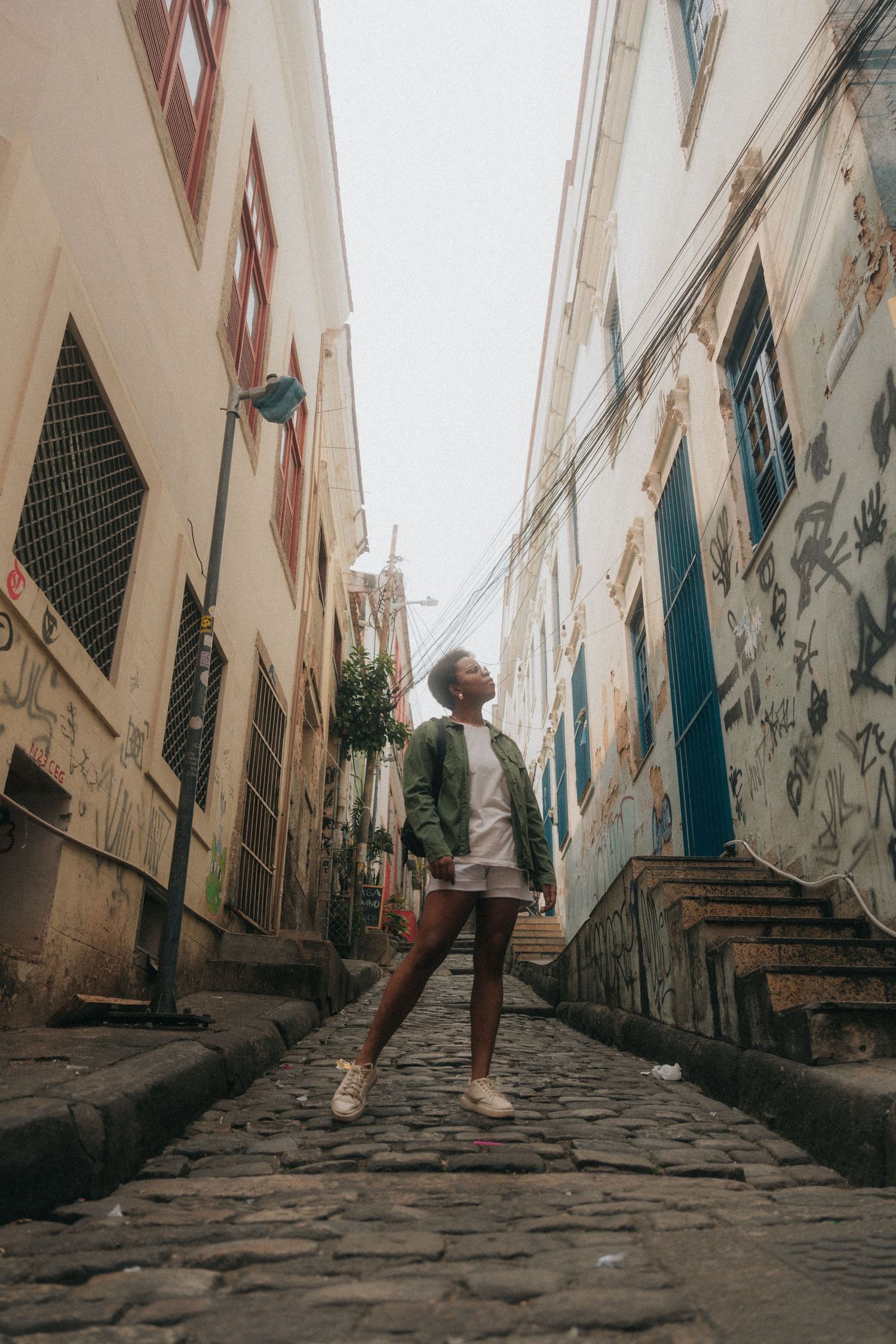 A person stands on a narrow cobblestone street between tall buildings in Salvador, Brazil.