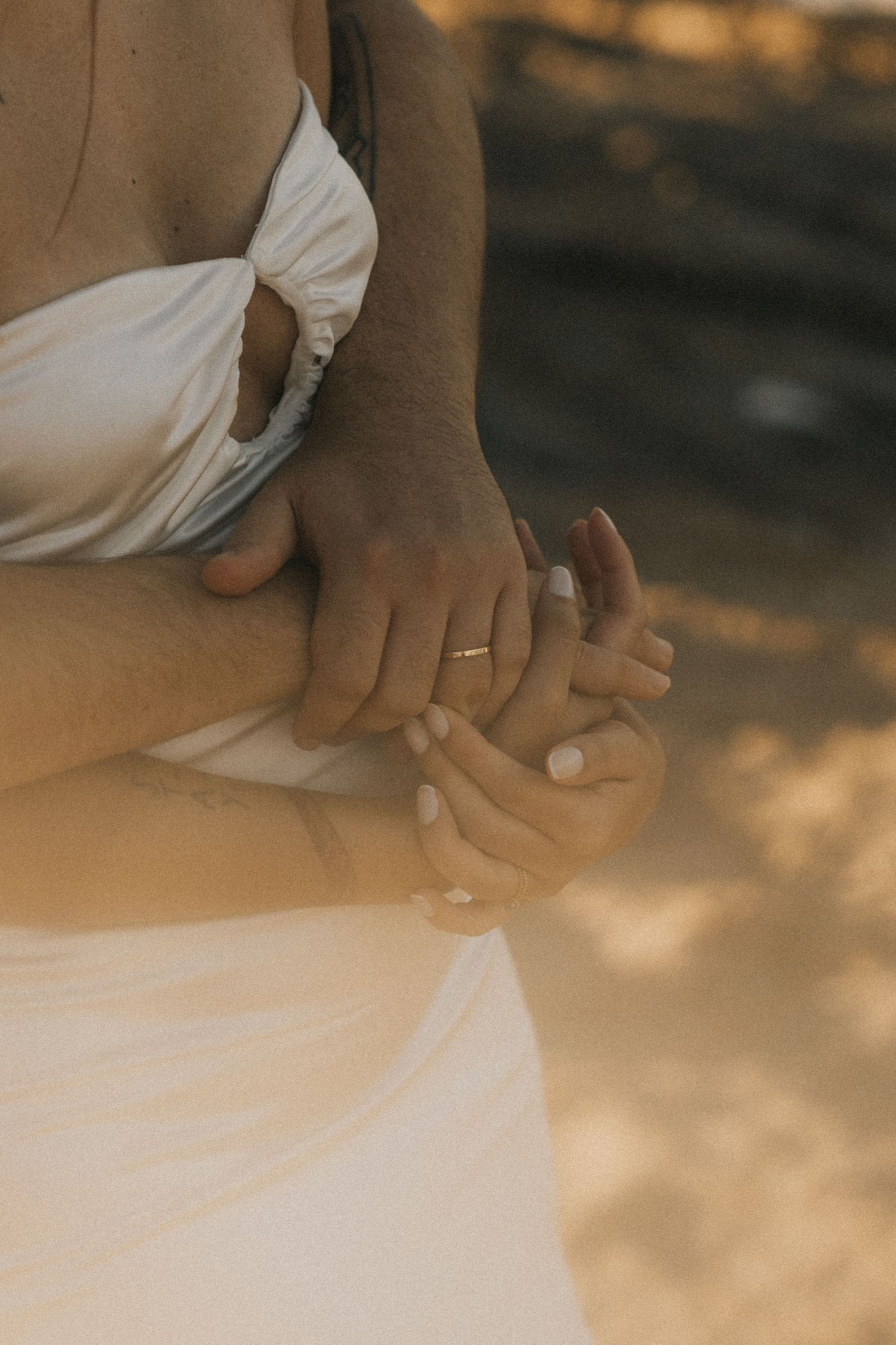 Close-up of hands clasping a white flowy dress fabric in soft golden sunlight.