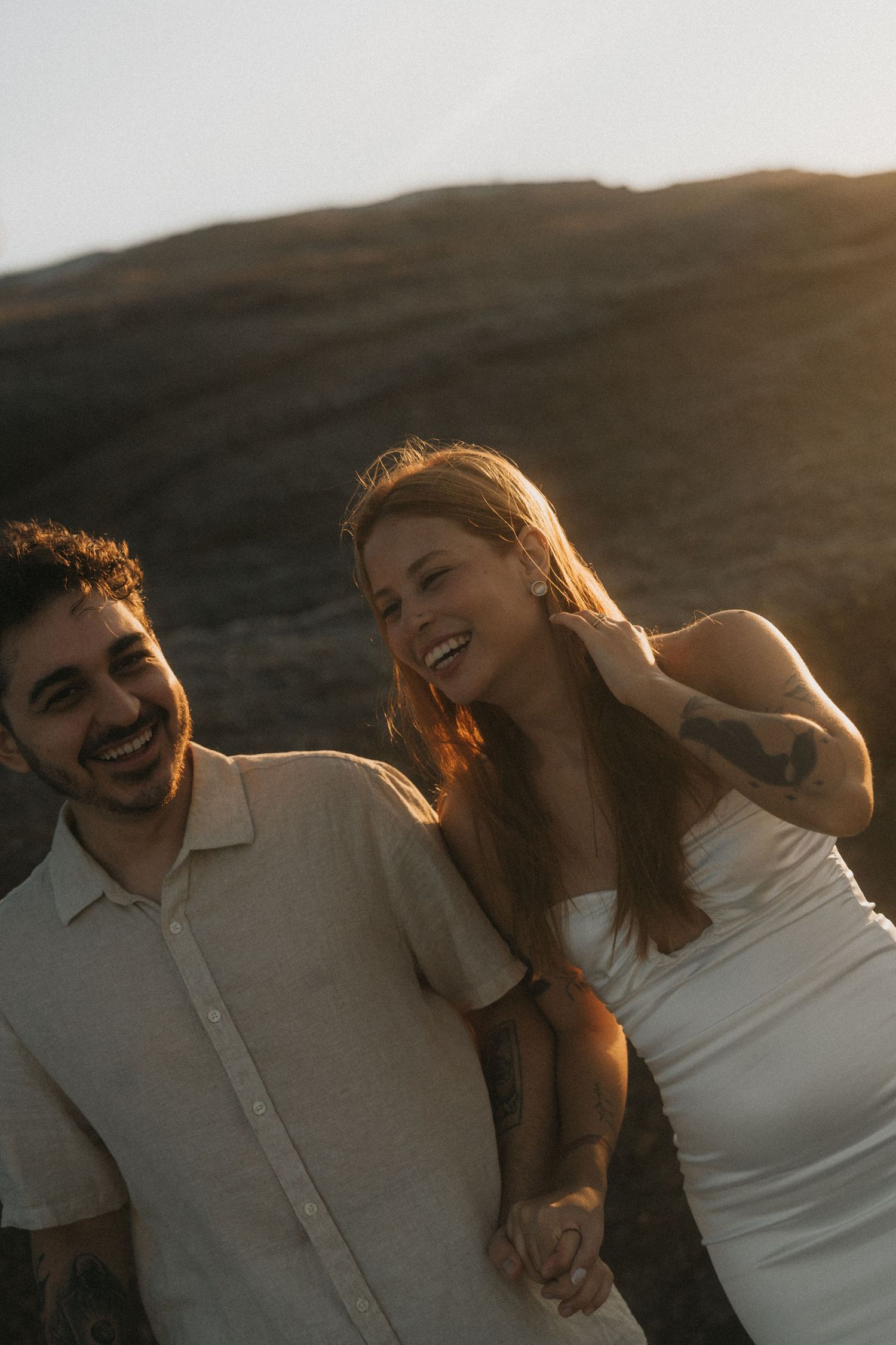 A couple laughs together during sunset photoshoot in golden hour lighting.