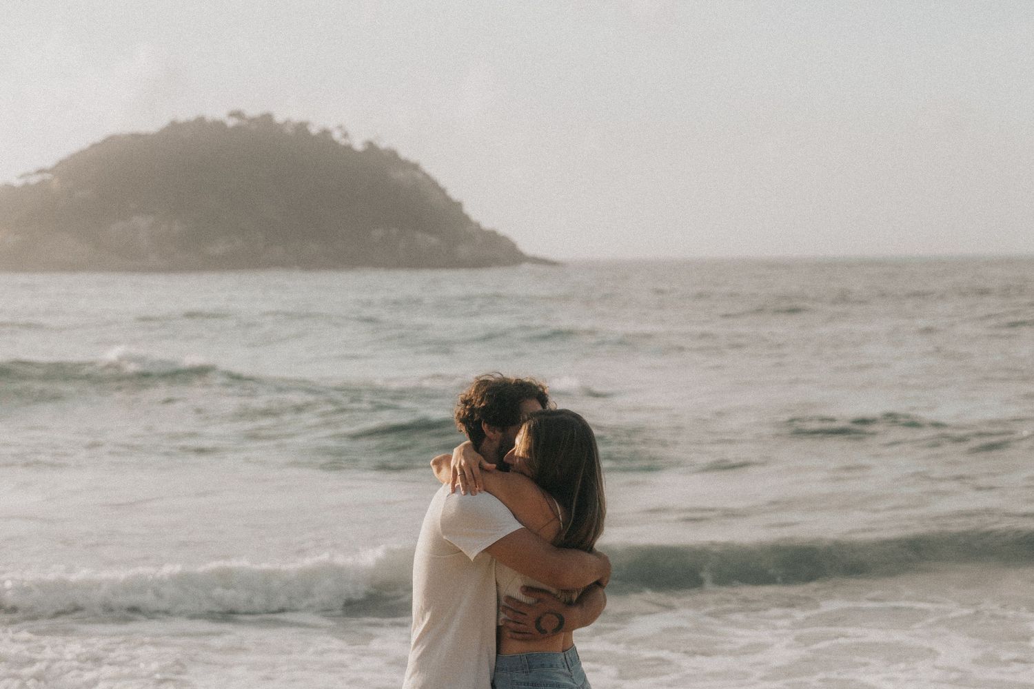 Series of romantic beach engagement photos capture couple embracing at seaside during golden hour.