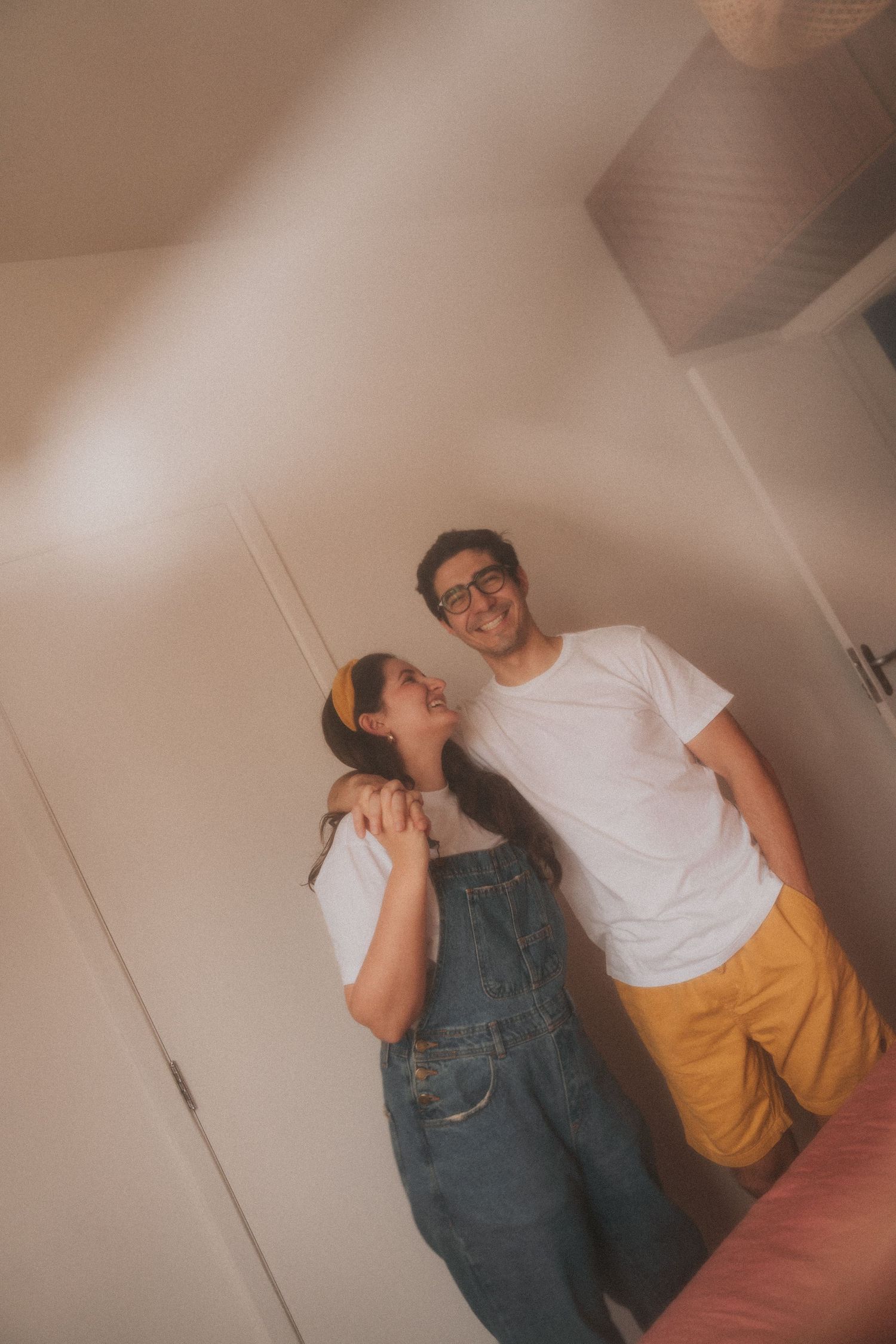 A couple in casual outfits stands close together against a white wall in a sequence of romantic poses.