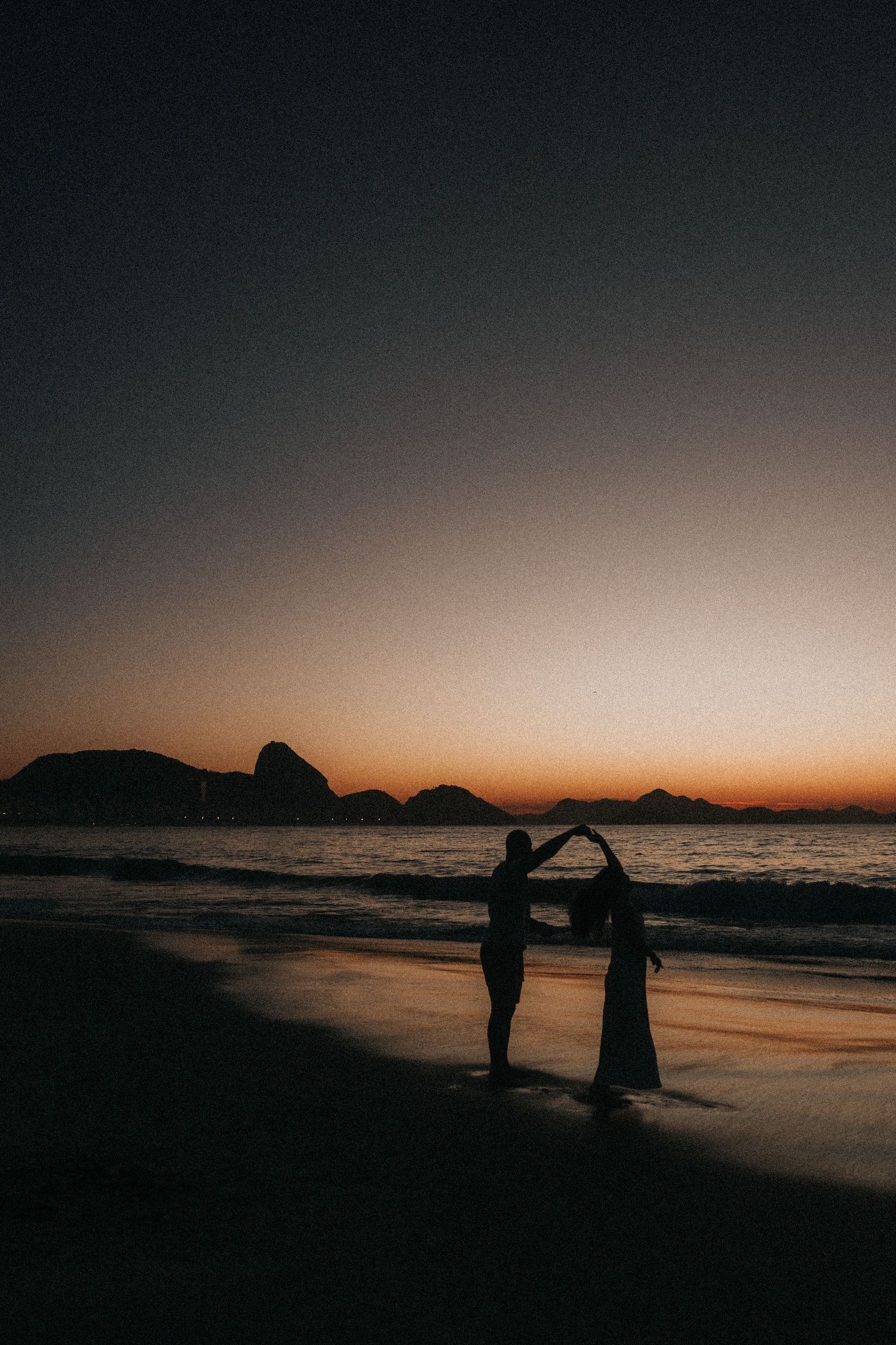 Silhouettes of figures captured against a dramatic beach sunset creating romantic coastal shadows on the shoreline.